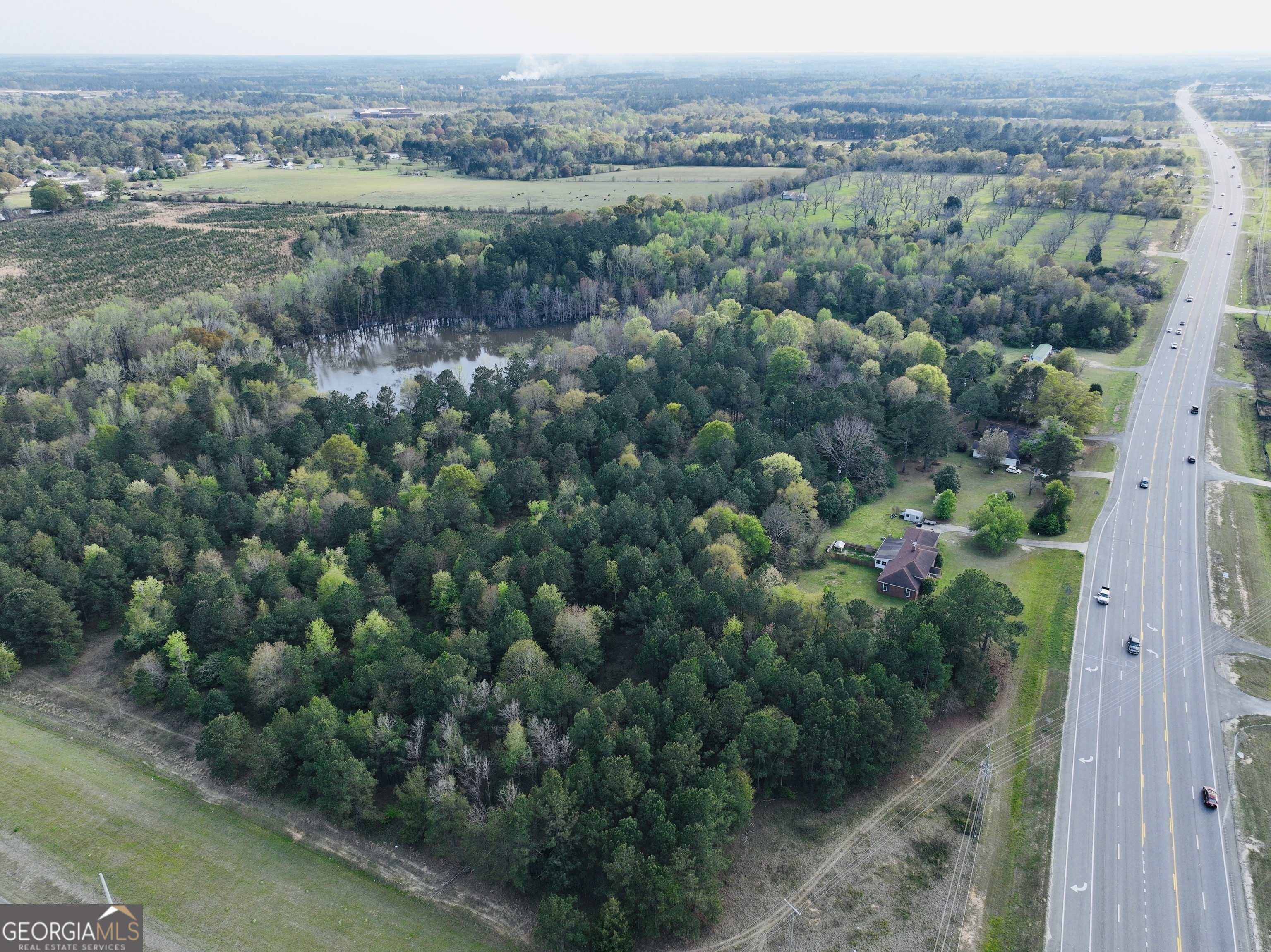 Aerial view of wooded property with a pond and house beside a multi-lane highway.