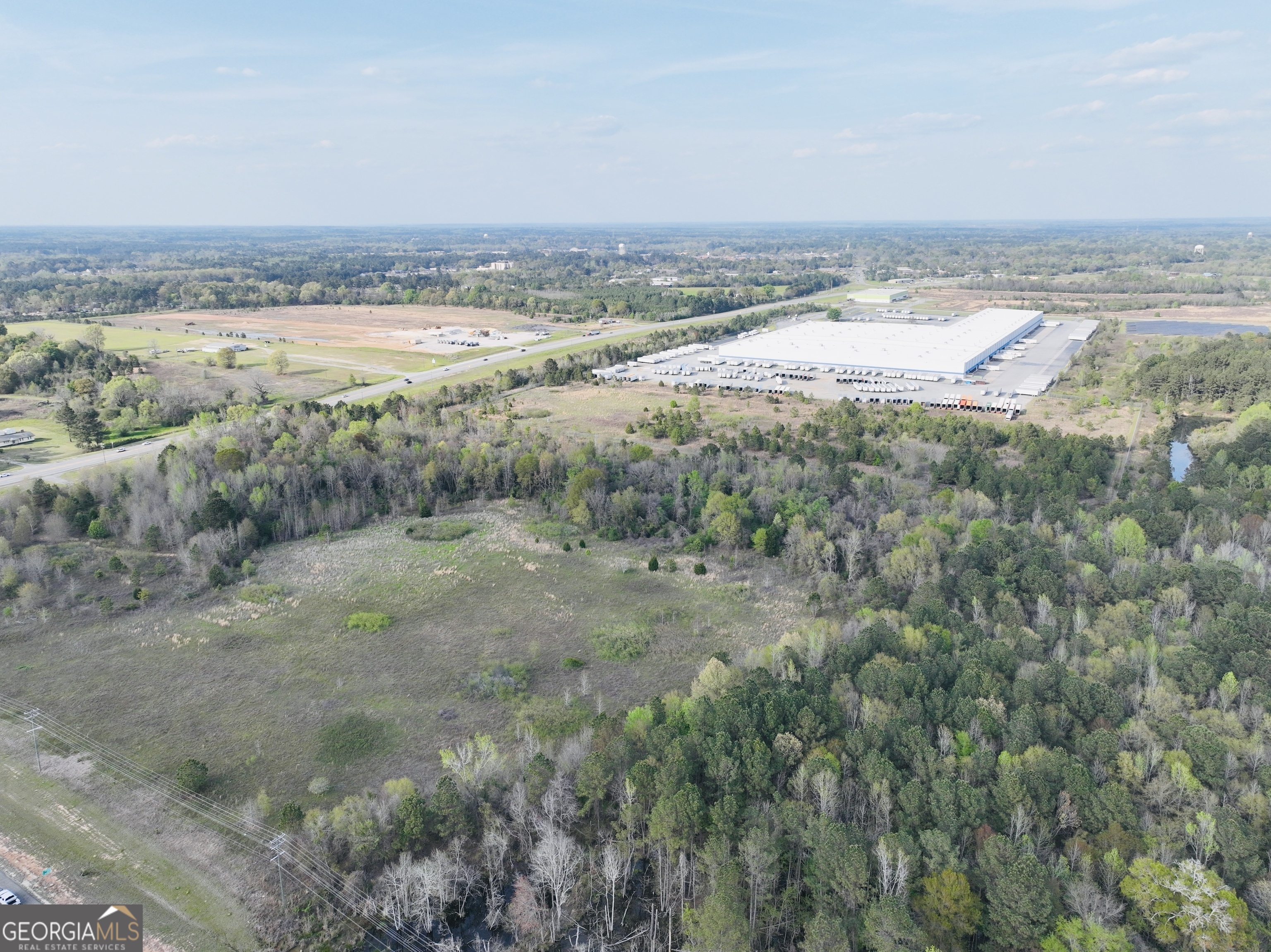 Aerial view of wooded and cleared land beside a highway, with a large warehouse nearby.