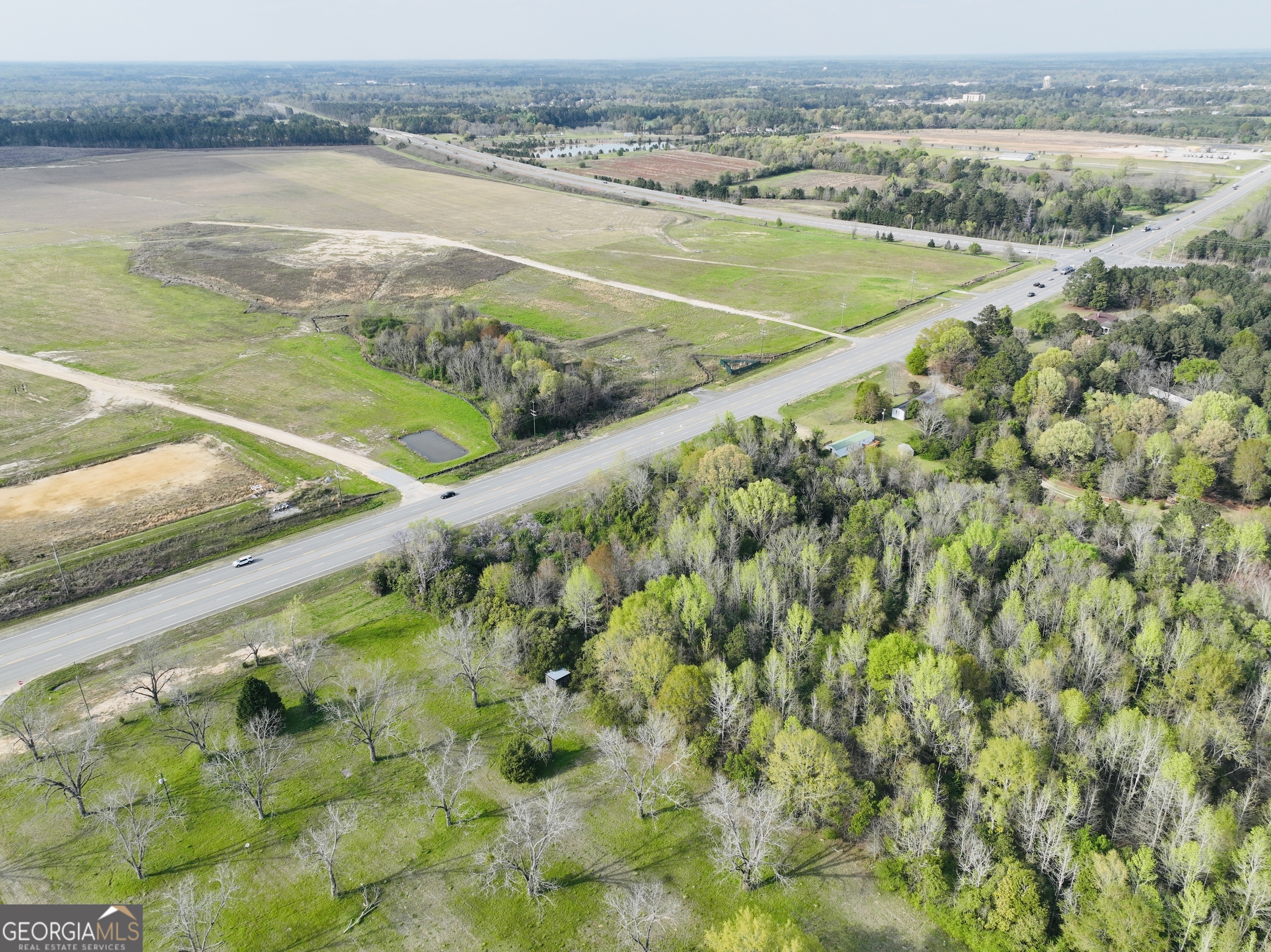 Aerial view of open fields and wooded land beside a highway.