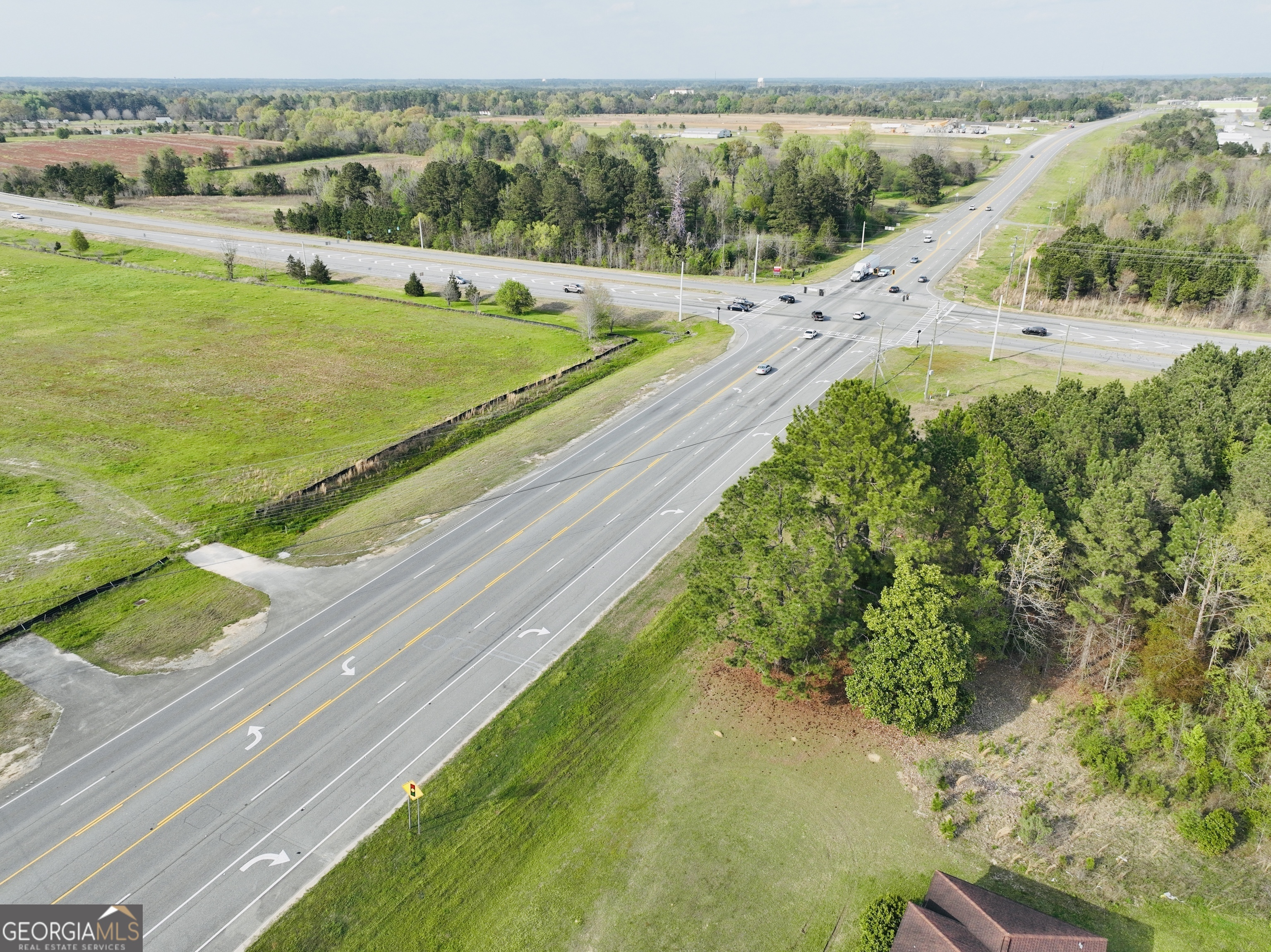 Aerial view of grassy land beside a highway intersection, with wooded edges and nearby commercial buildings.