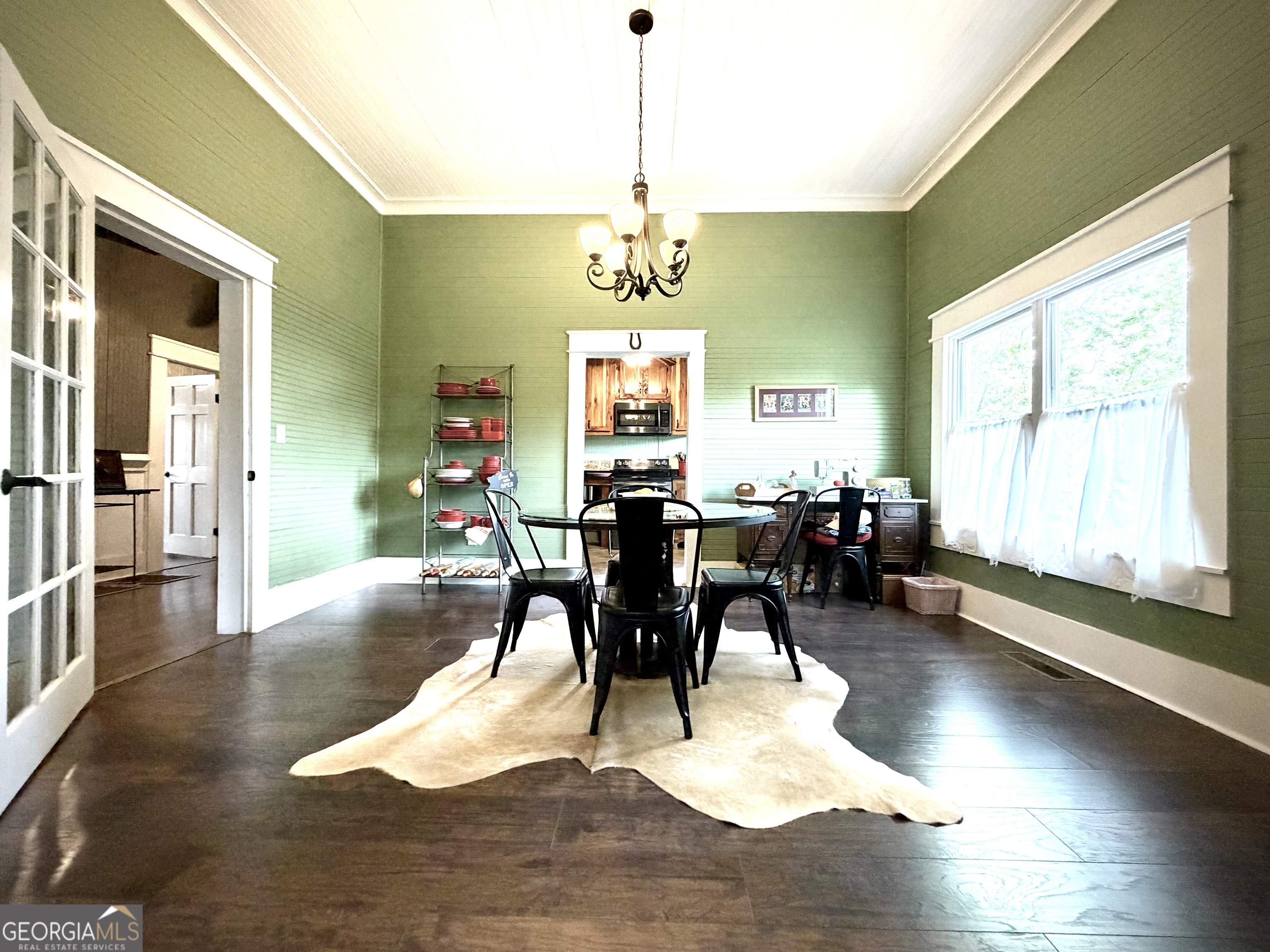 Dining room with sage-green walls, a black table and chairs, chandelier, and kitchen beyond.