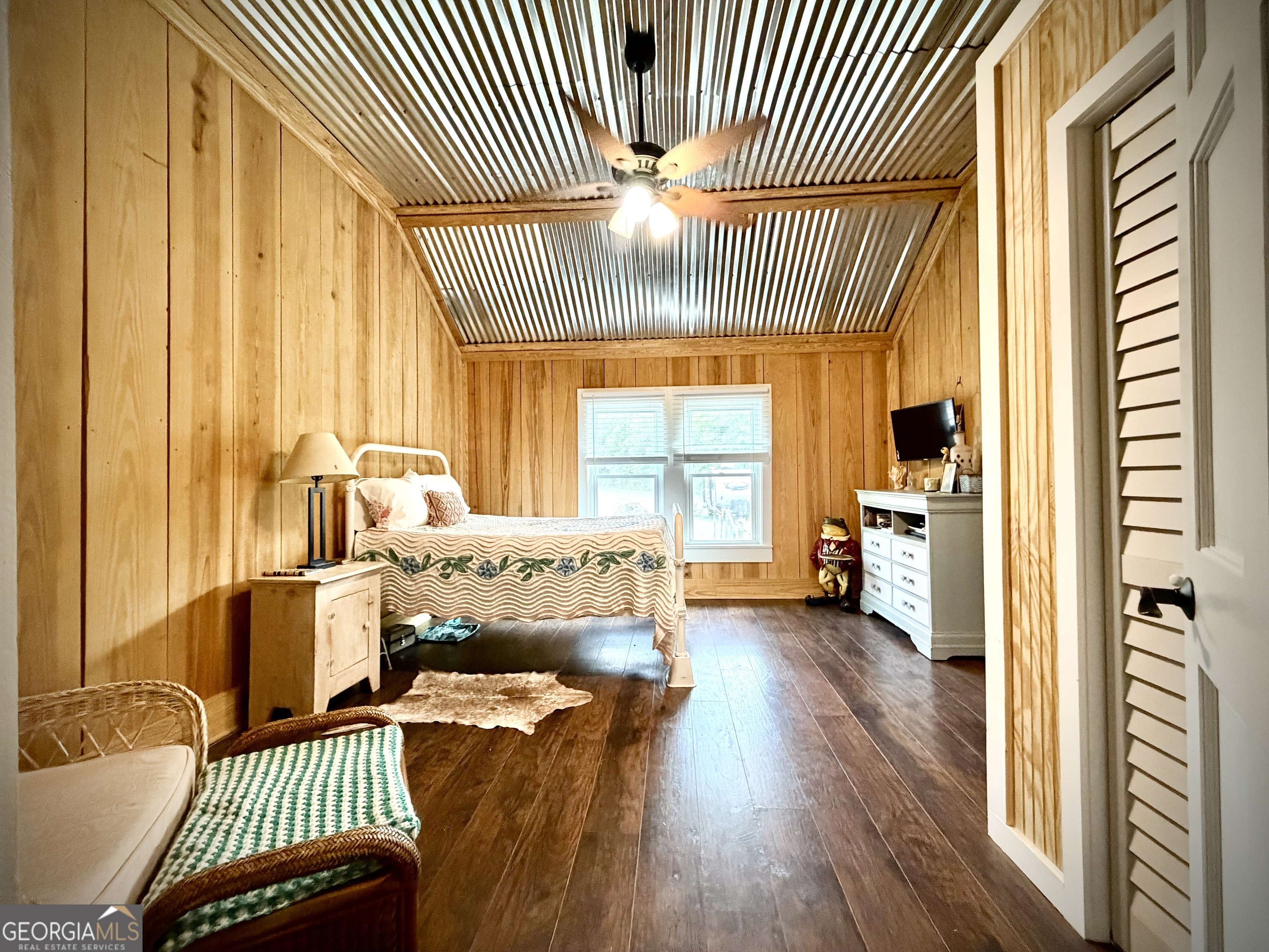 Bedroom with a corrugated metal ceiling, wood-paneled walls, and a bed beneath the window.