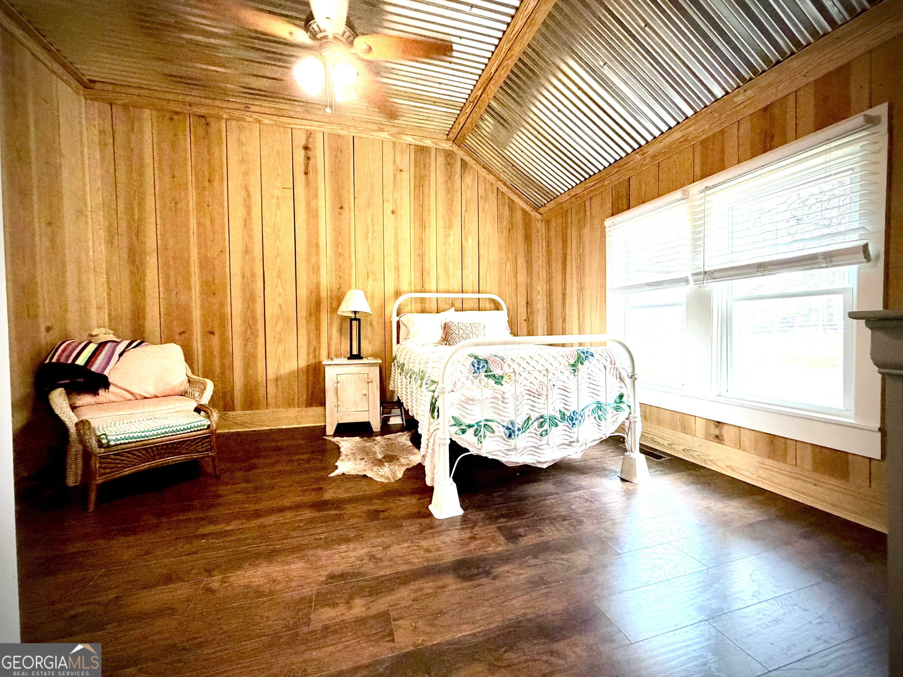 Bedroom with wood-paneled walls, a vaulted metal ceiling, and a white bed beside large windows.