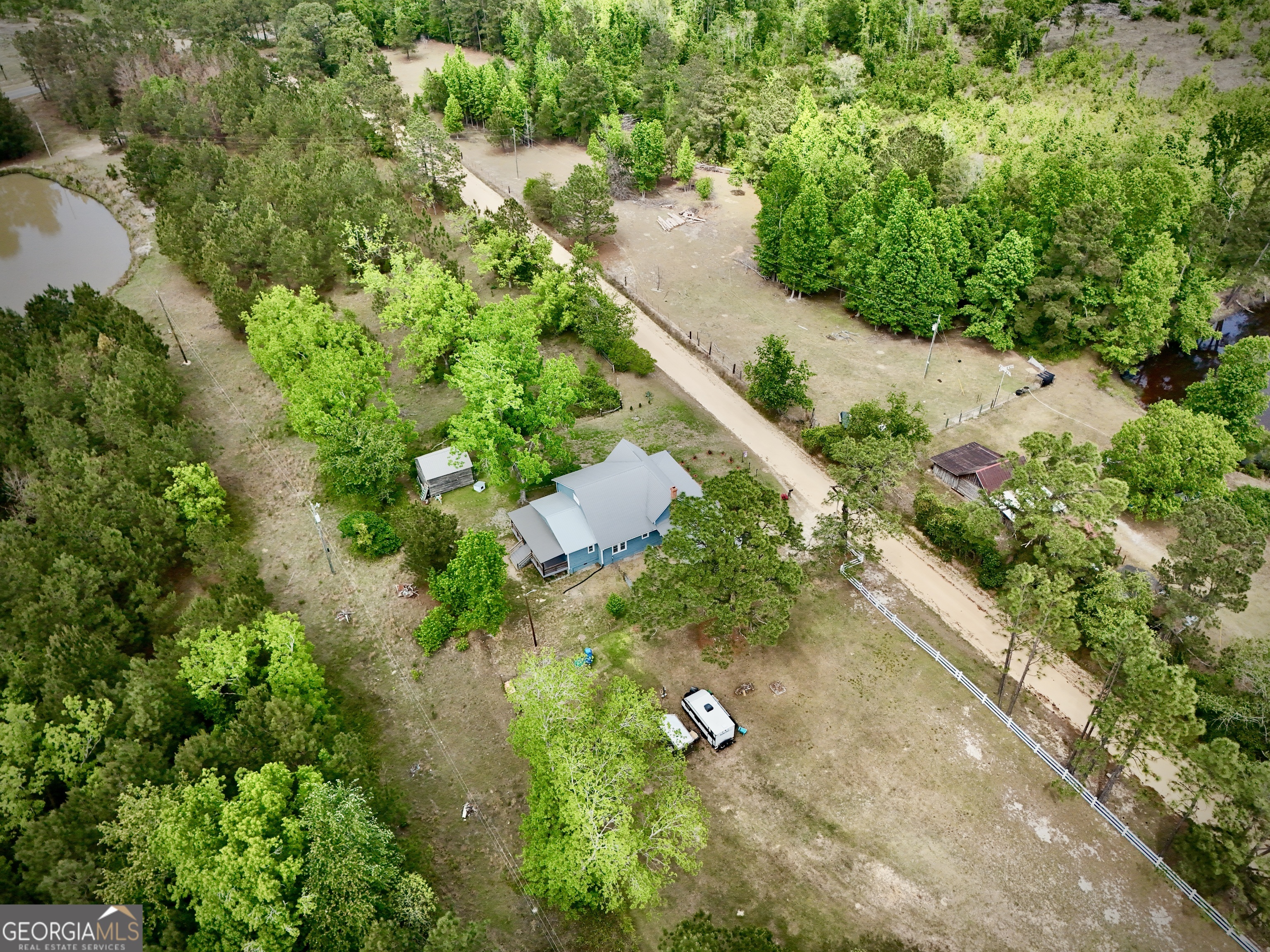 Aerial view of a rural home surrounded by trees, acreage, ponds, and a dirt road.