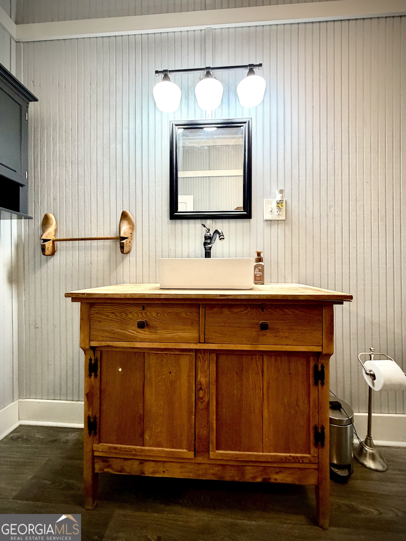 Bathroom vanity with a rustic wooden cabinet, white vessel sink, and black-framed mirror.