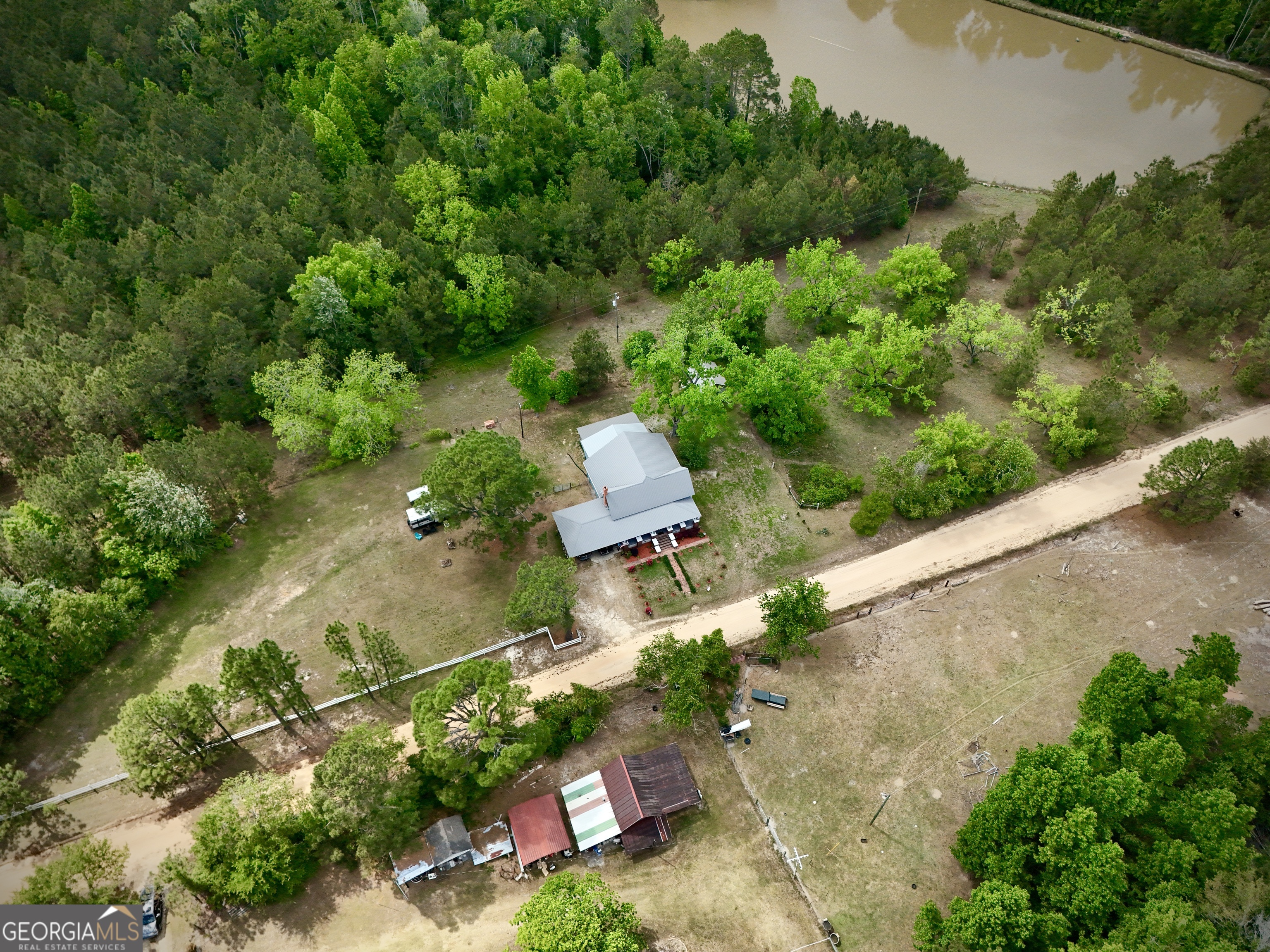 Aerial view of a rural home surrounded by trees, with outbuildings and a pond nearby.