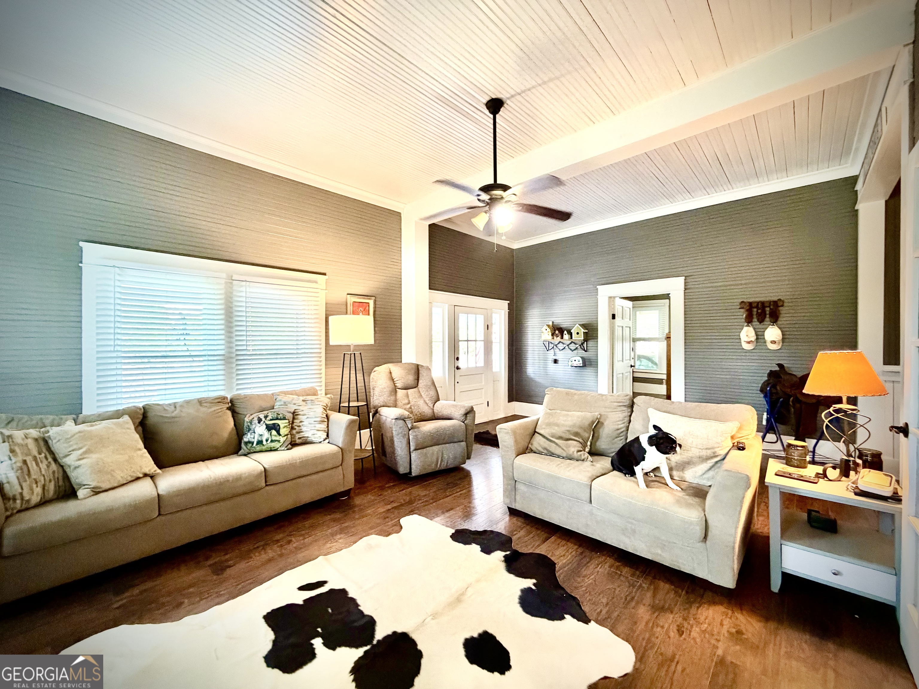 Living room with a high beadboard ceiling, neutral seating, and a black-and-white dog.