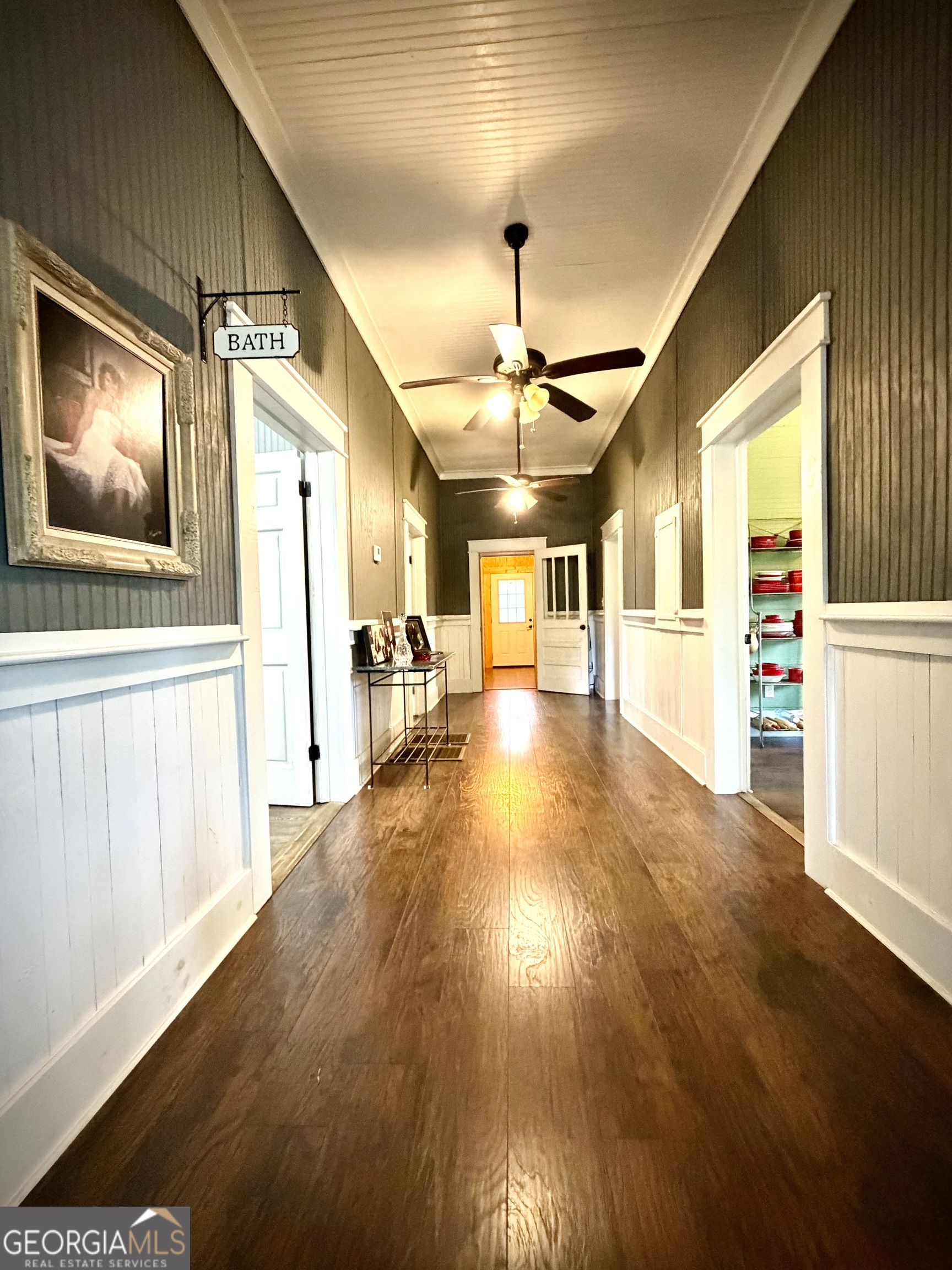 Long paneled hallway with dark wood floors, ceiling fans, and a yellow door at the far end.