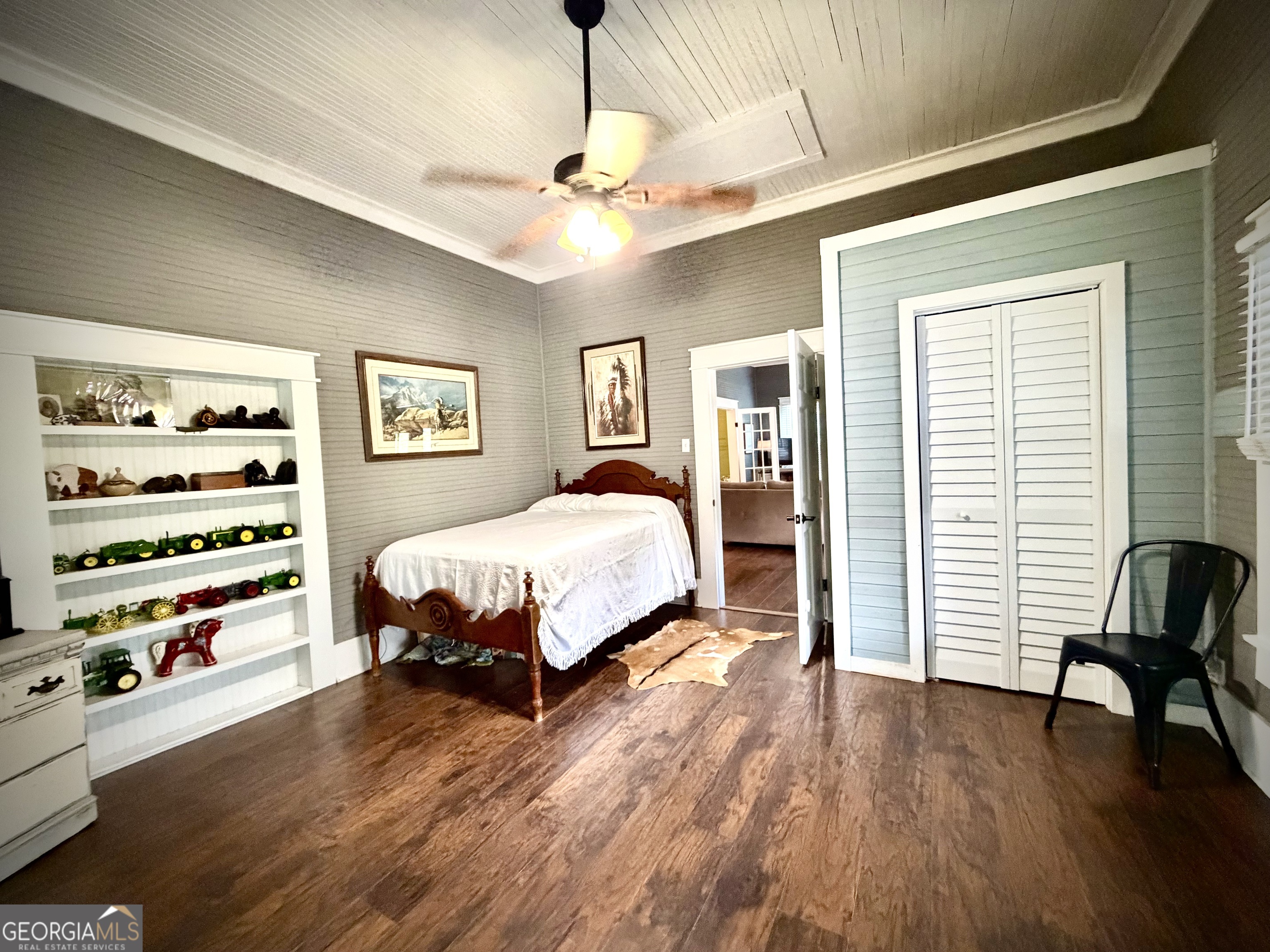 Bedroom with carved wooden bed, model tractors on built-in shelves, and white louvered closet doors.