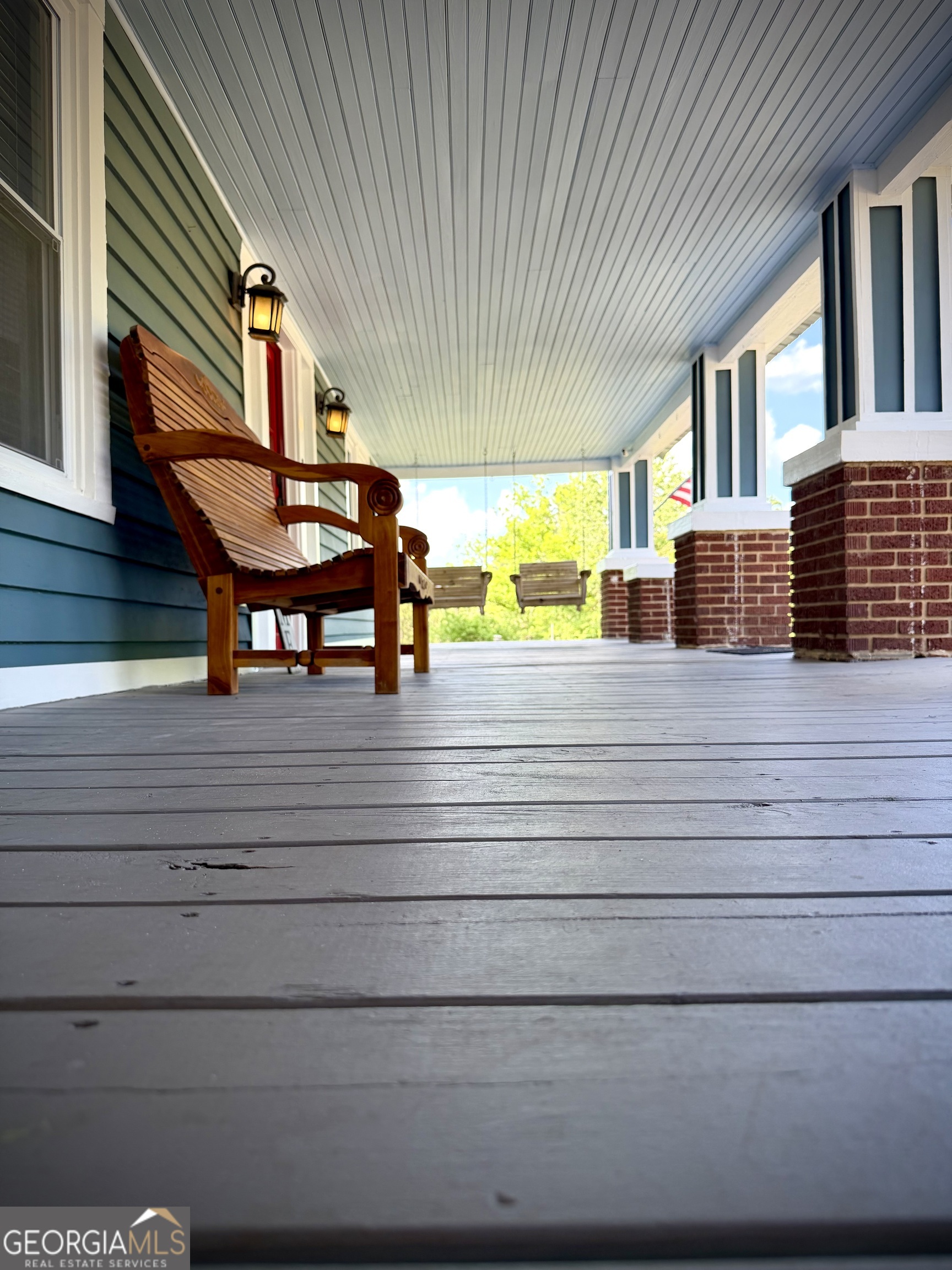 Covered front porch with wooden chairs, brick columns, and gray plank flooring.
