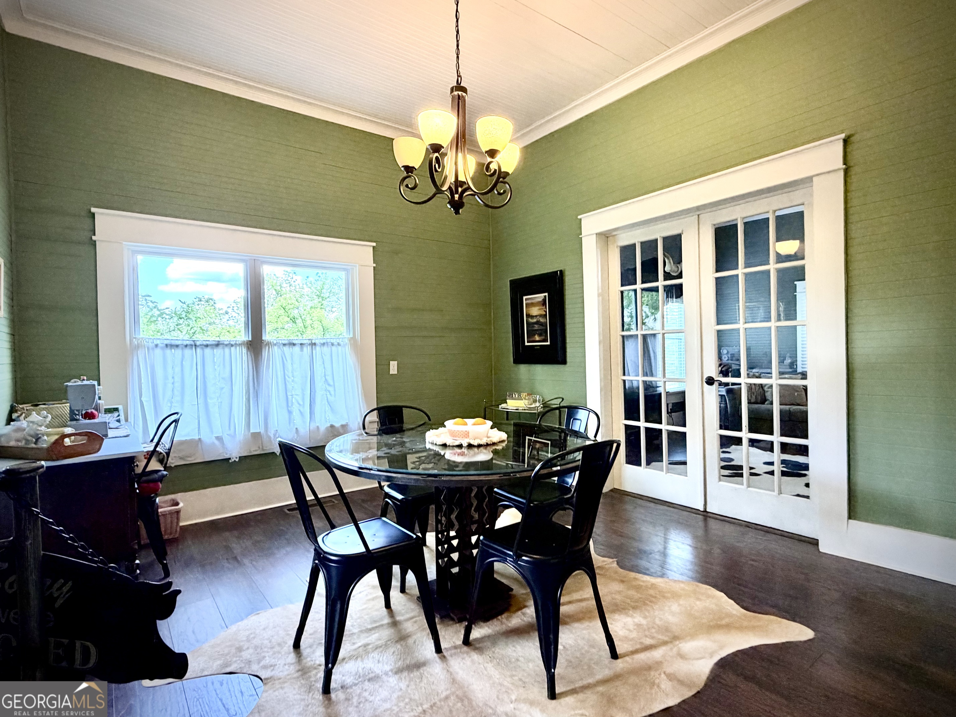 Dining room with a glass-top table, black chairs, green walls, and white French doors.