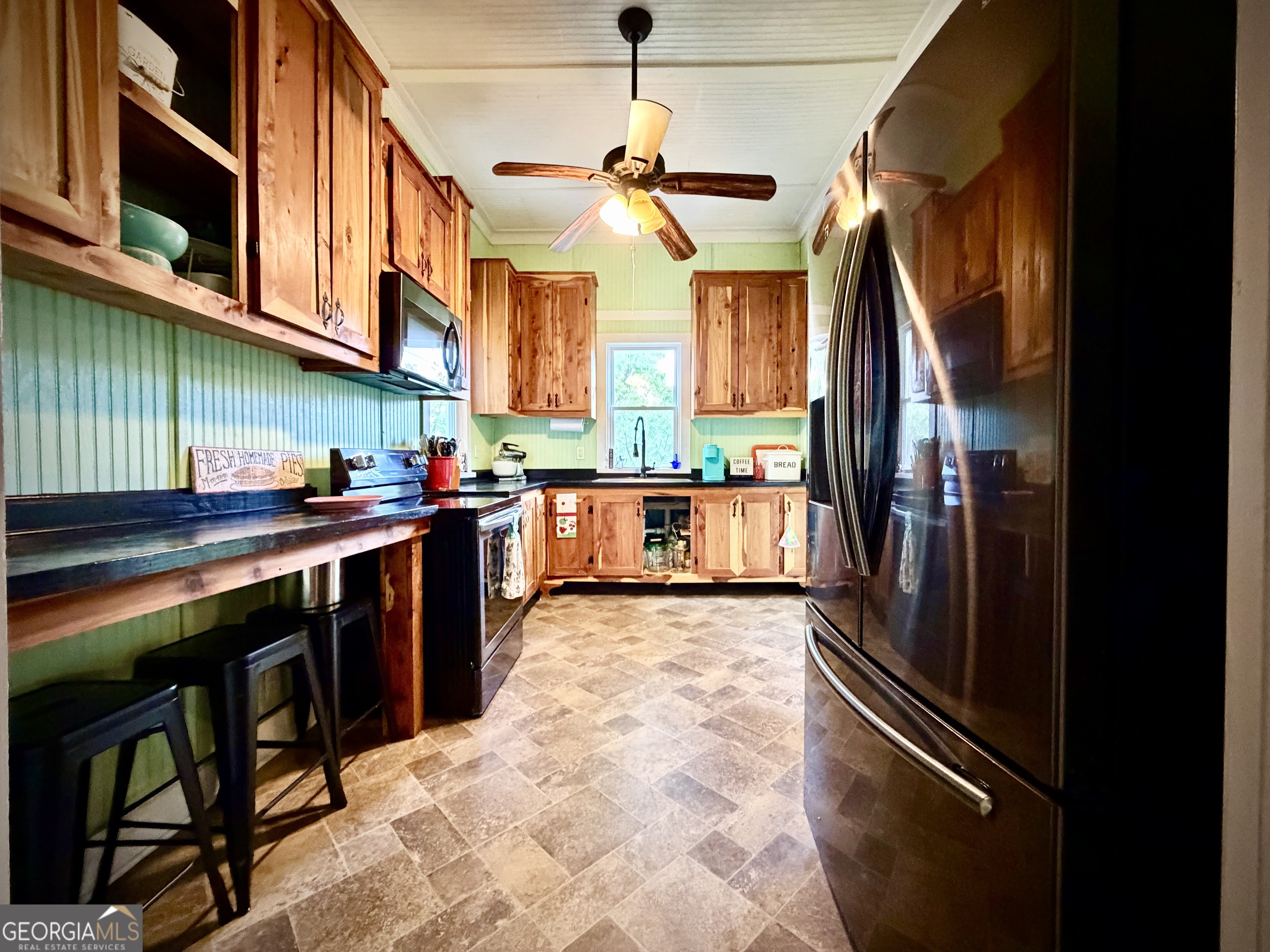 Kitchen with rustic wood cabinets, green beadboard walls, stainless steel appliances, and a breakfast bar.