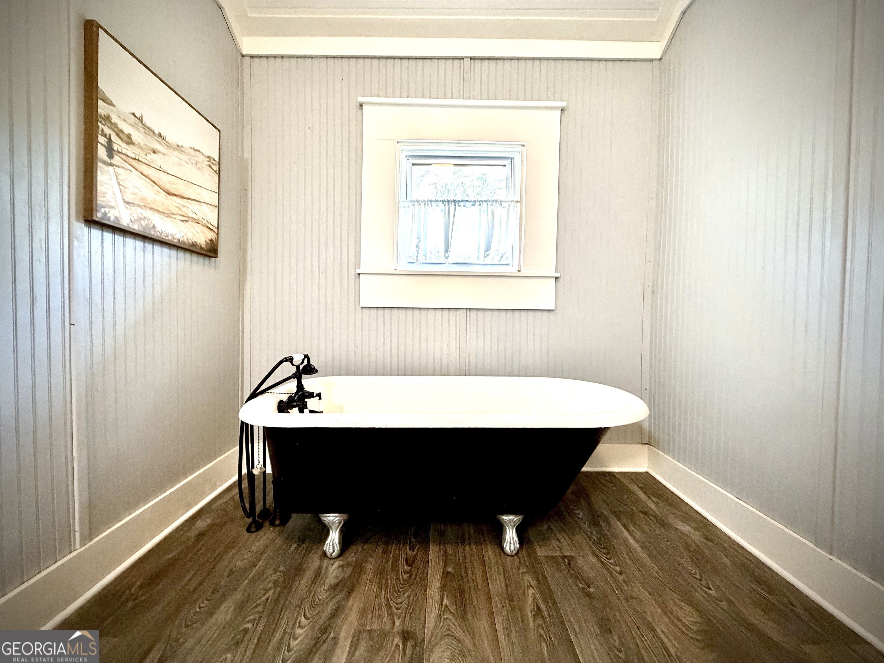 Bathroom with a black-and-white clawfoot tub beneath a small curtained window.