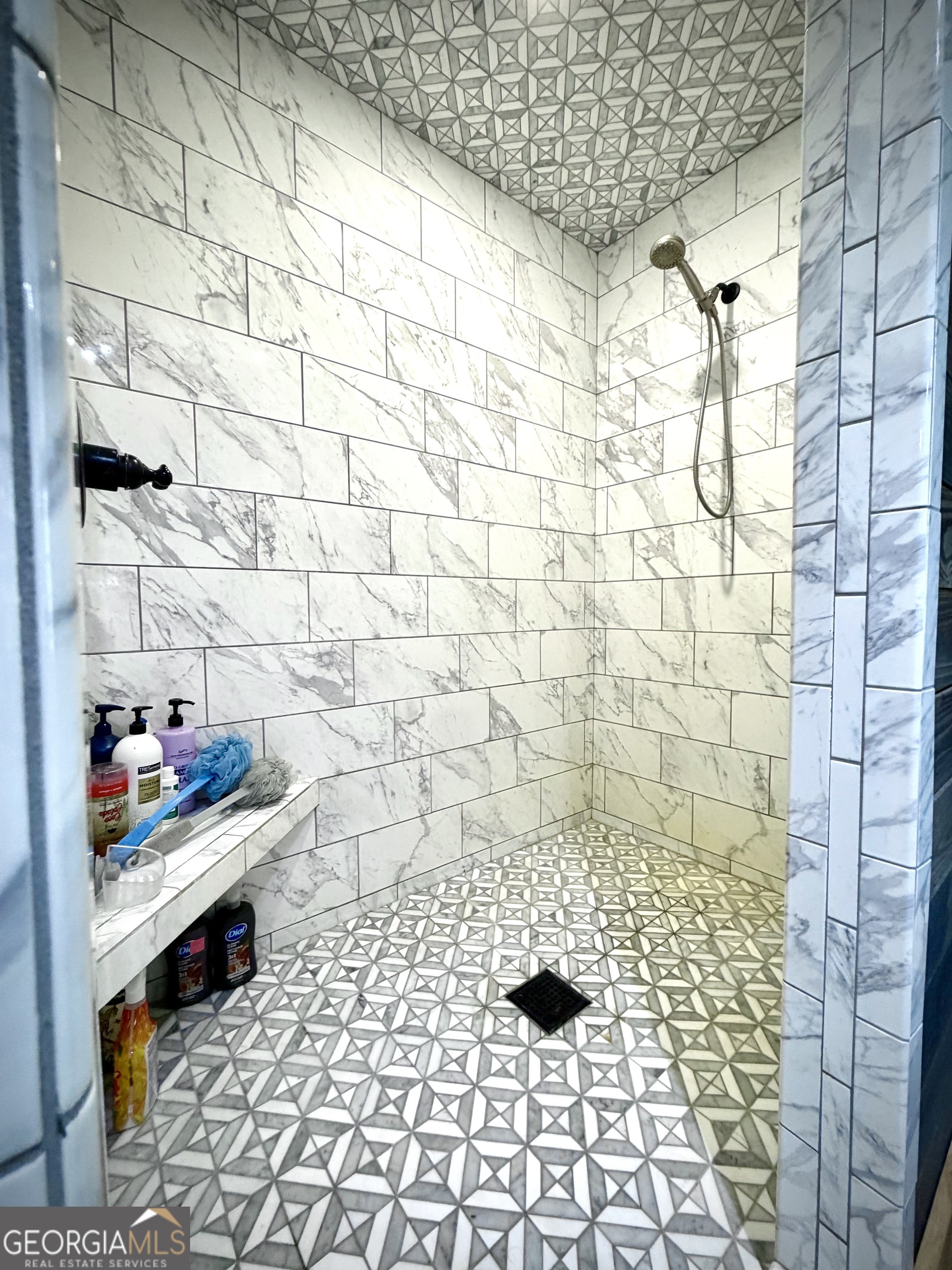 Walk-in shower with marble-look walls and bold geometric tile across the ceiling and floor.