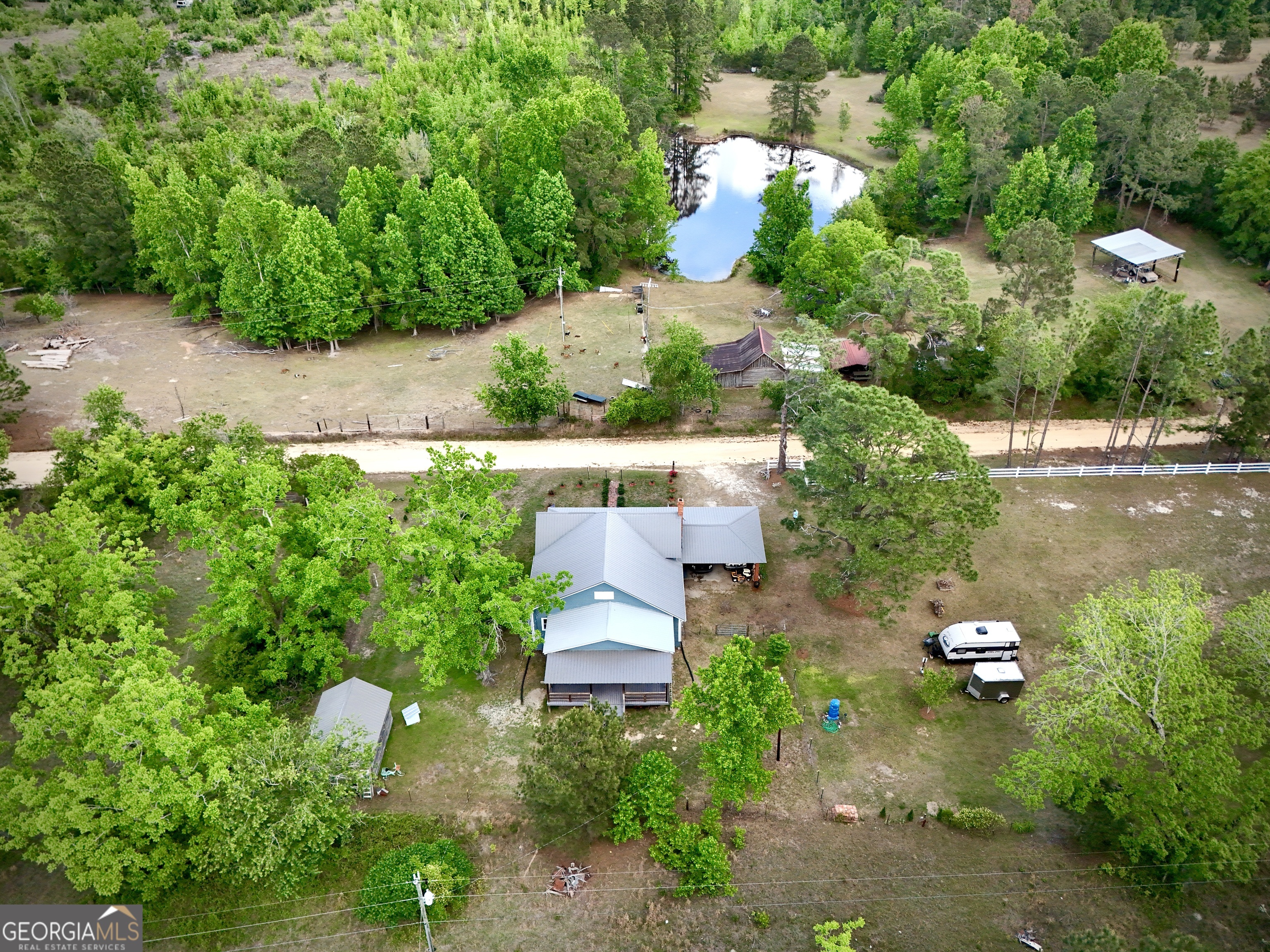 Aerial view of a rural home and wooded acreage with a pond and outbuildings.