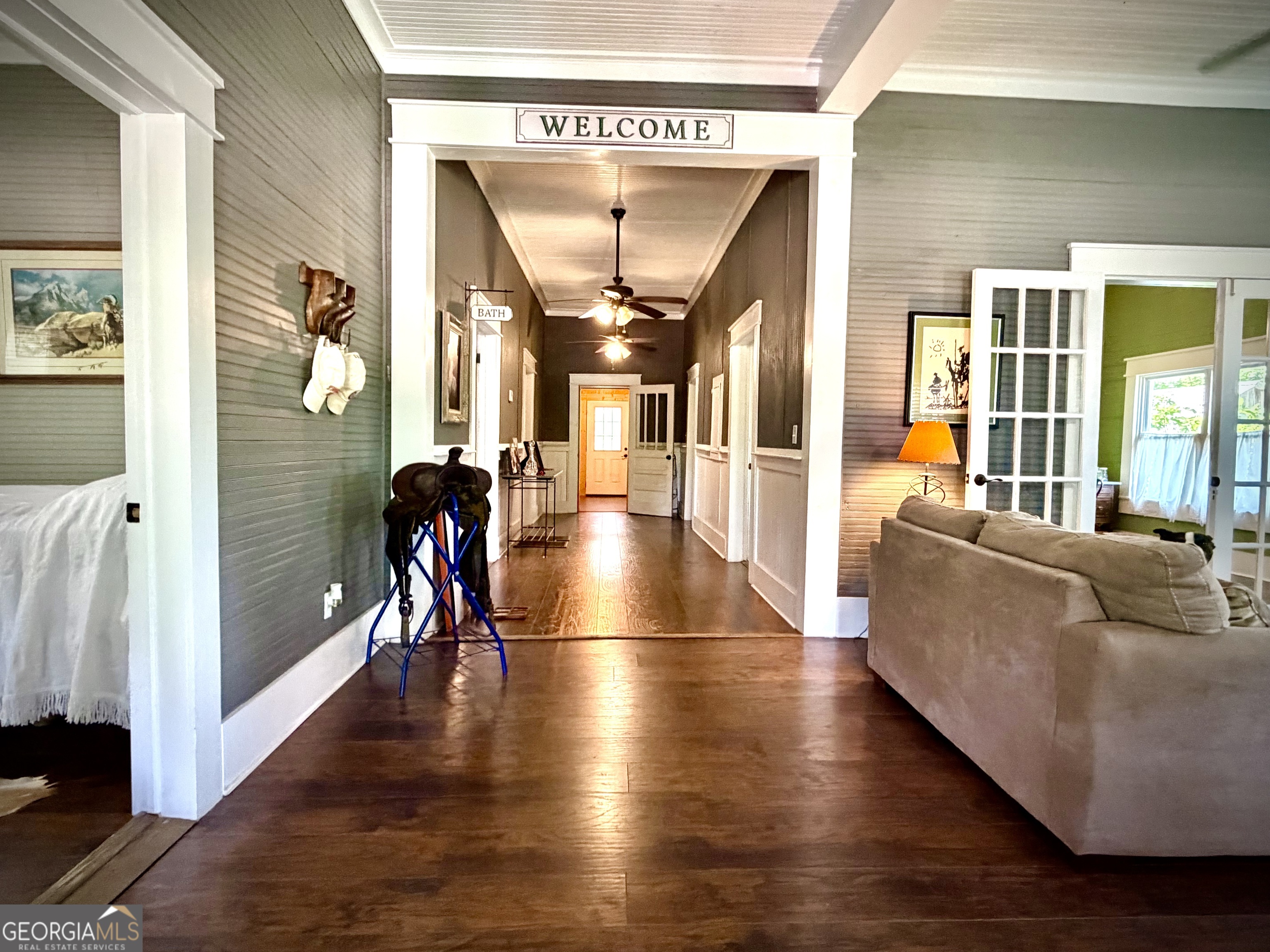 Furnished hallway with dark wood floors, ceiling fans, and an adjacent living area with a sofa.