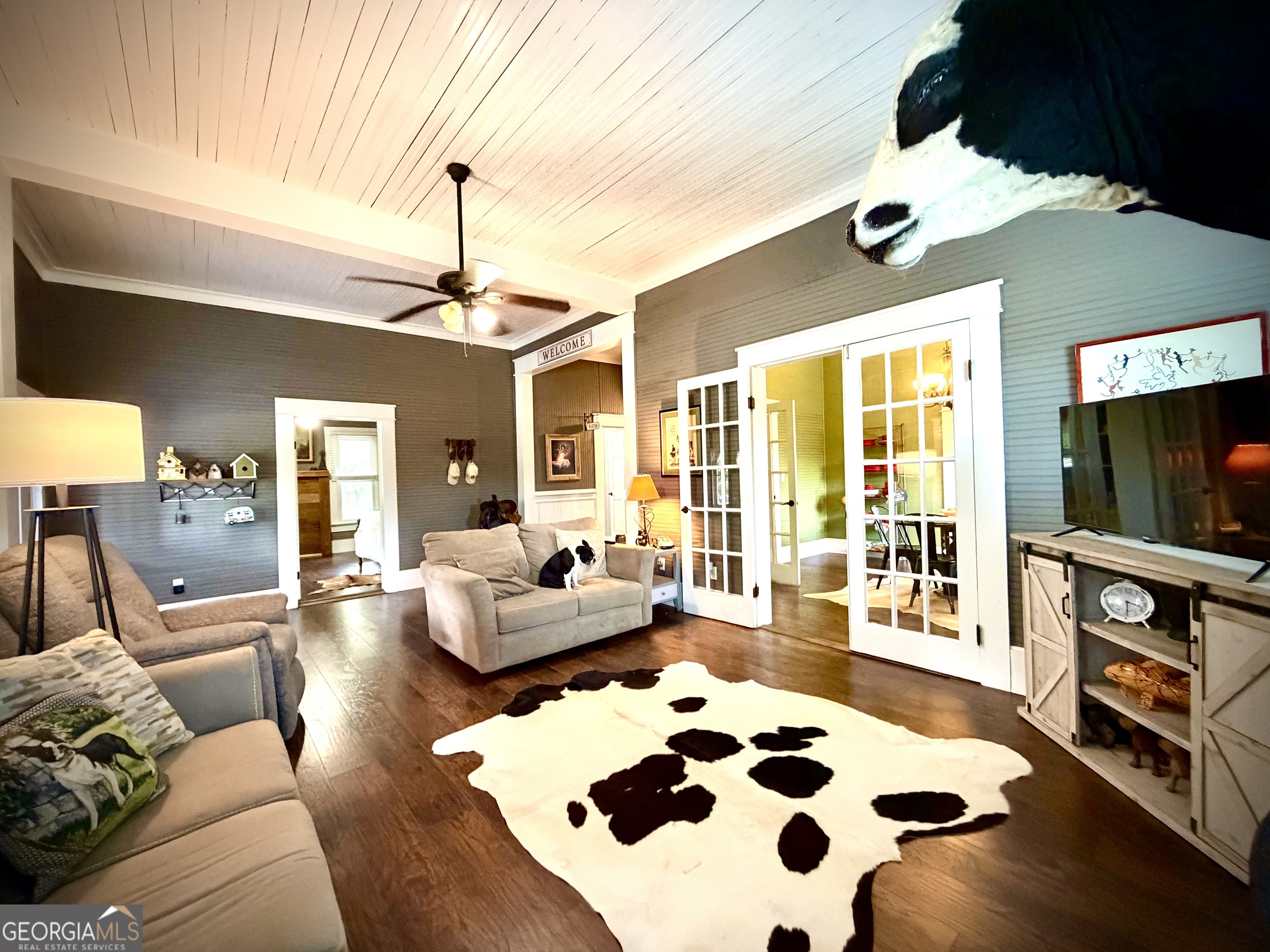 Furnished living room with French doors, a cowhide rug, a dog on the sofa, and a mounted cow head.