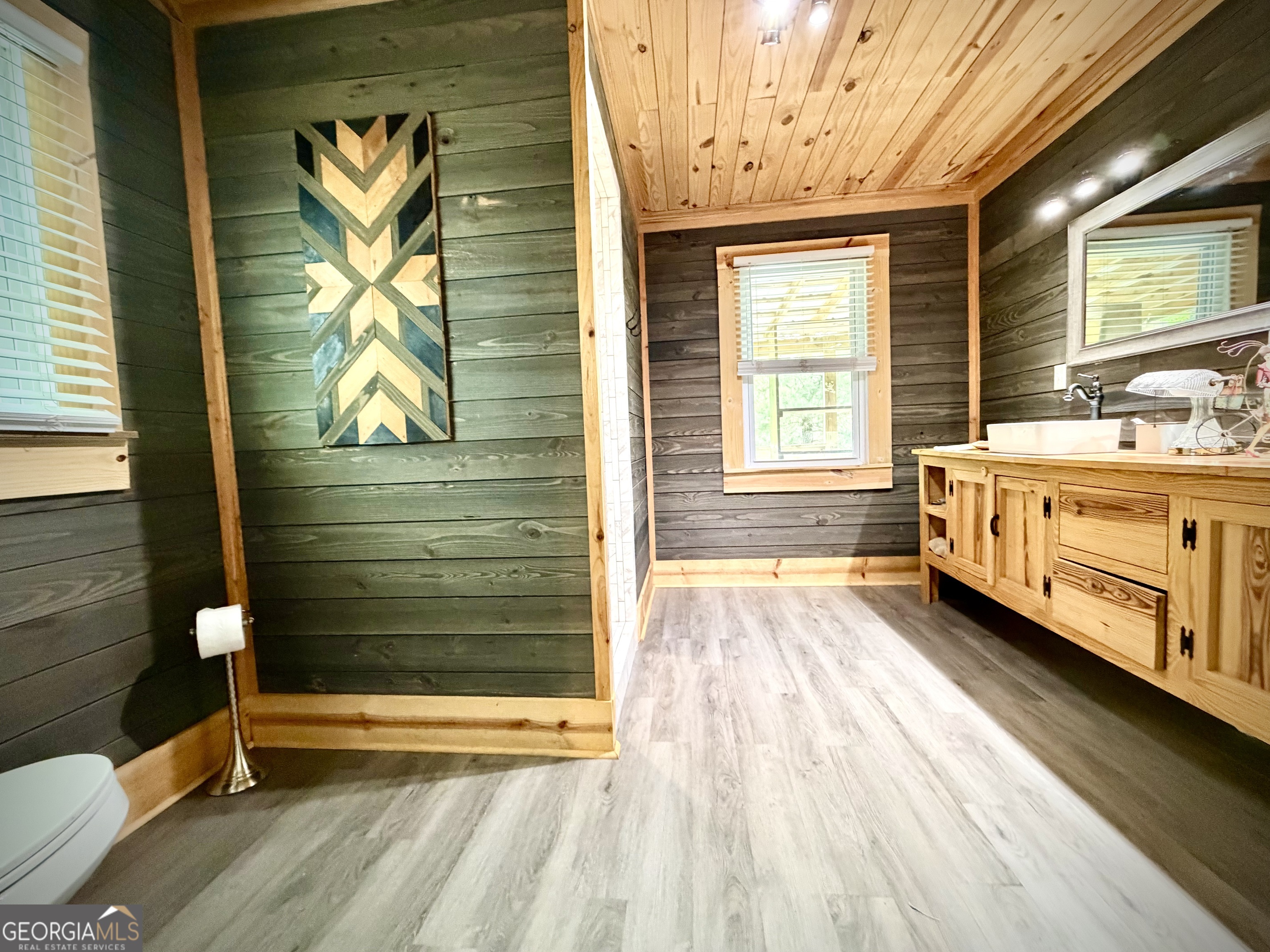Bathroom with a knotty-pine ceiling, dark wood walls, and a long natural-wood vanity.