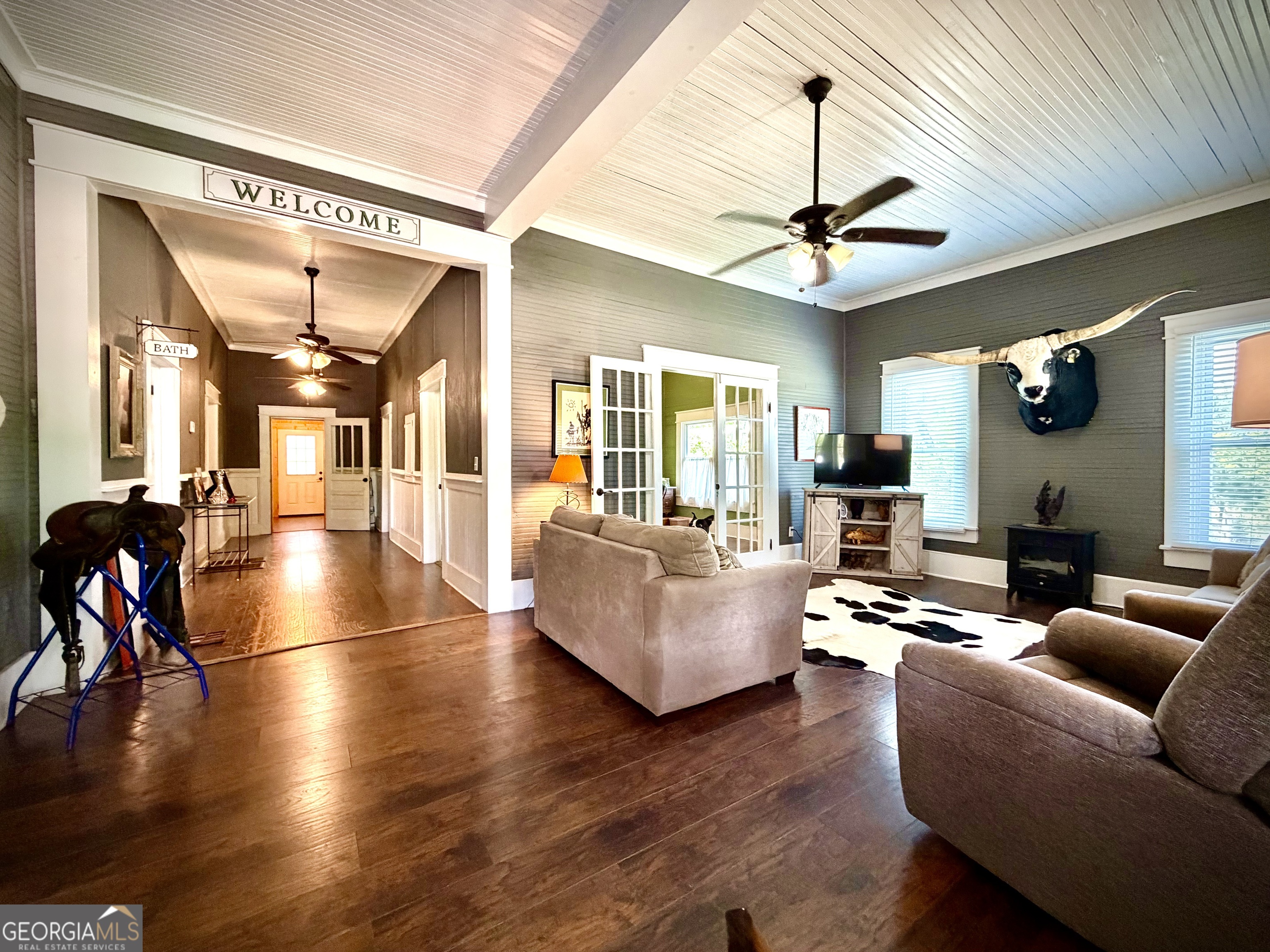 Furnished living room with dark wood floors, French doors, and a mounted longhorn head.