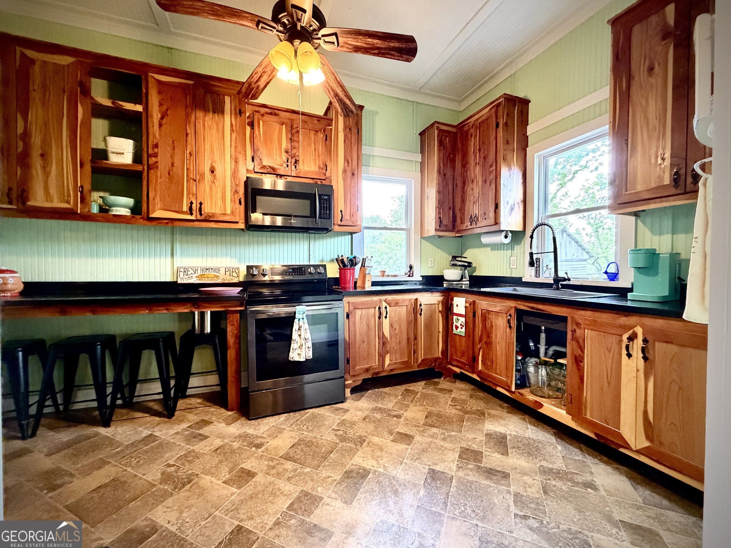 Kitchen with warm wood cabinetry, green paneled walls, black countertops, and a breakfast bar with stools.