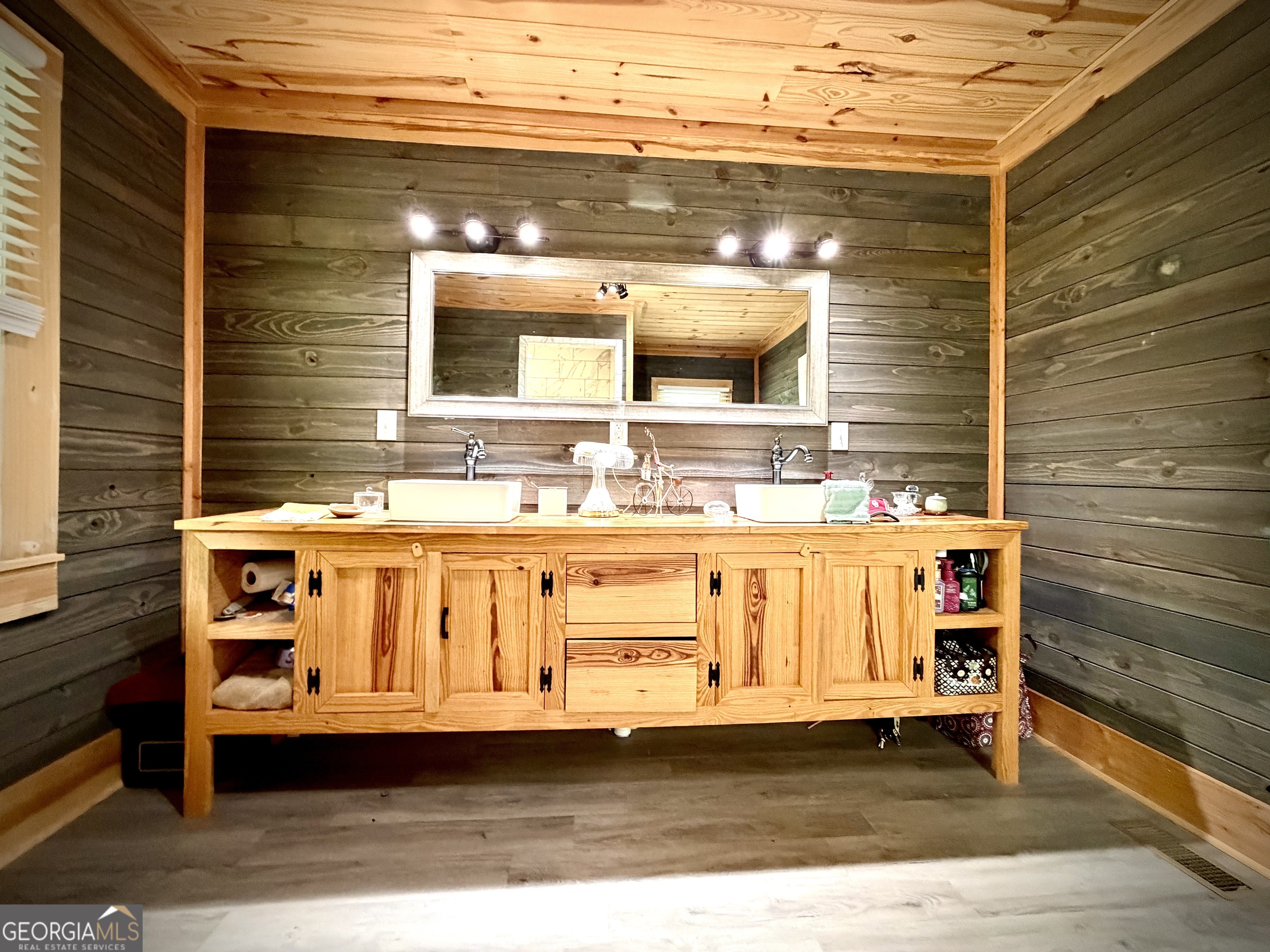 Bathroom with a long pine double vanity, vessel sinks, and dark wood-plank walls.