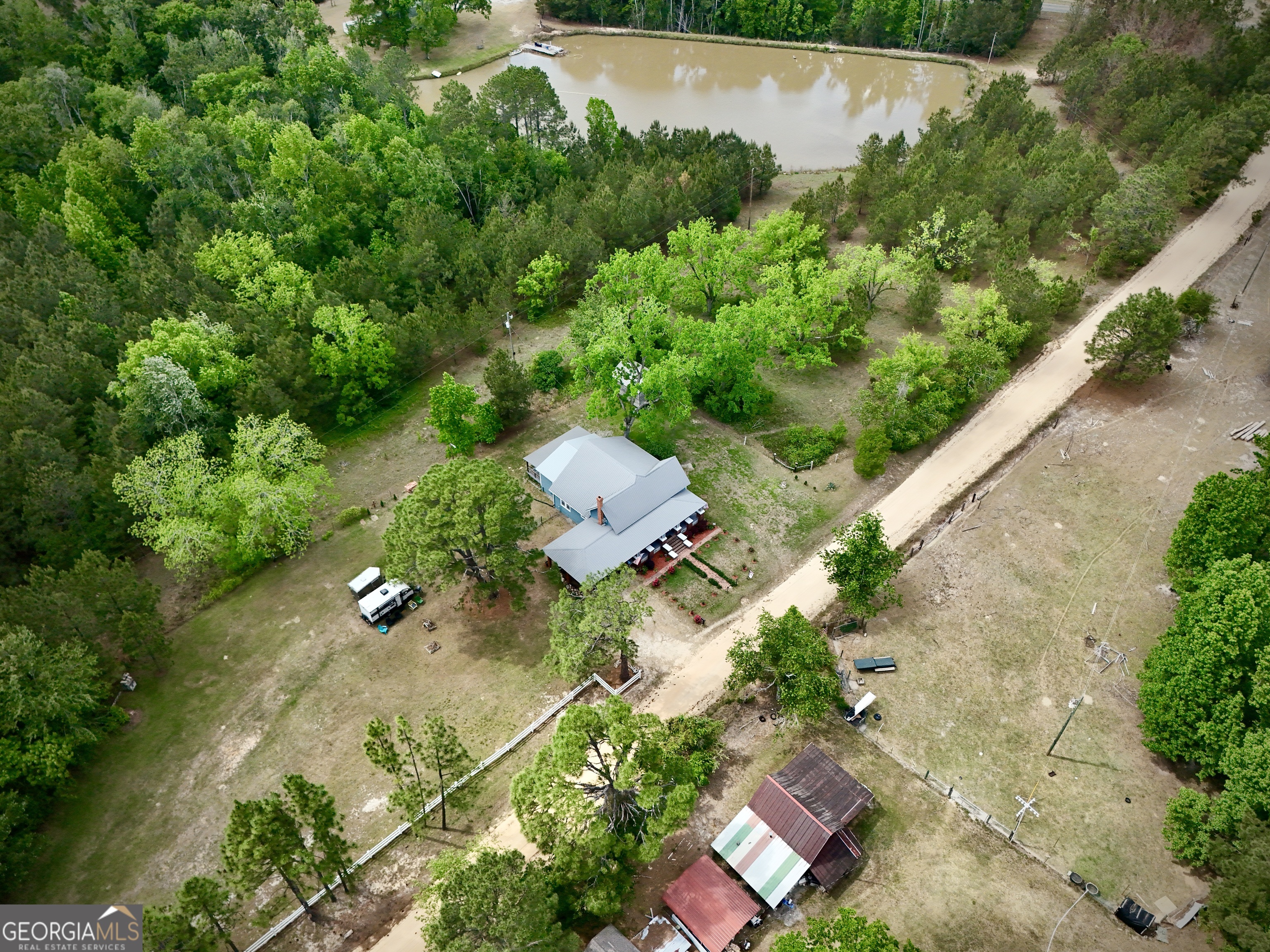Aerial view of a rural home surrounded by trees, outbuildings, and a pond.