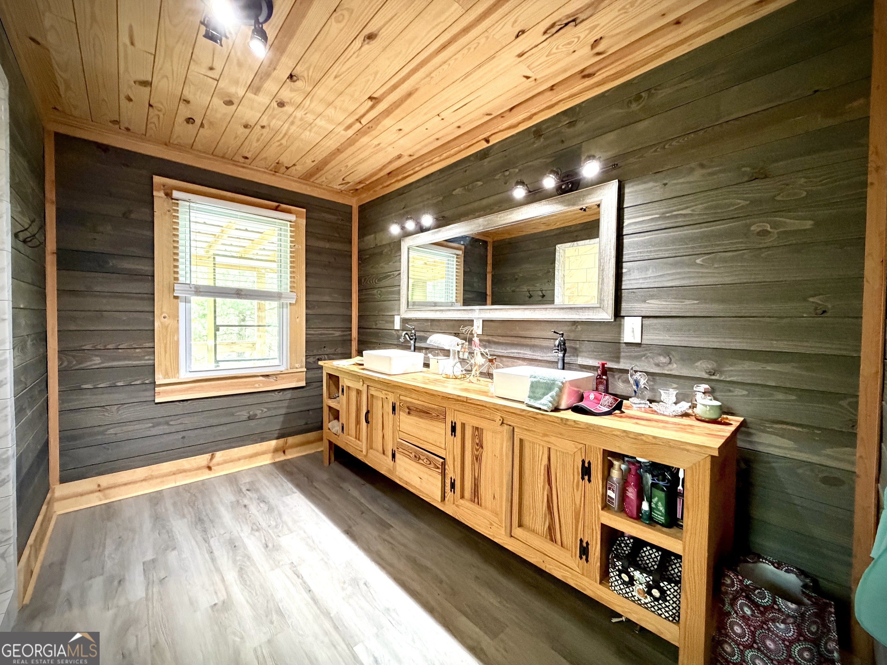 Bathroom with a long natural-wood double vanity, white vessel sinks, dark plank walls, and a wide mirror.