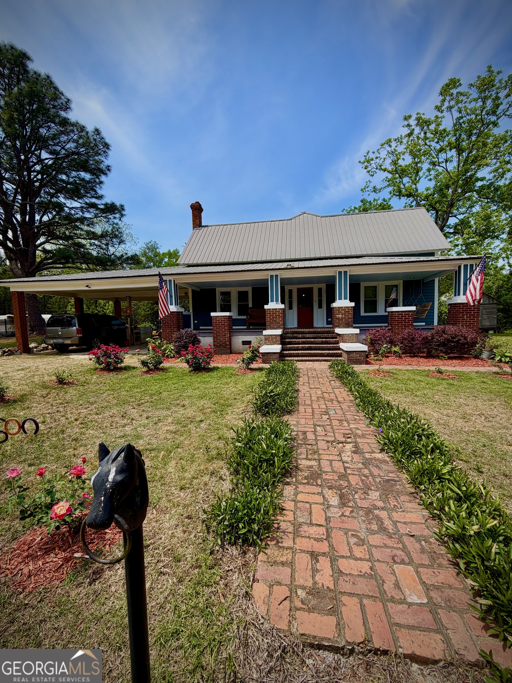 Blue house with a metal roof, brick porch, and flower-lined brick walkway.