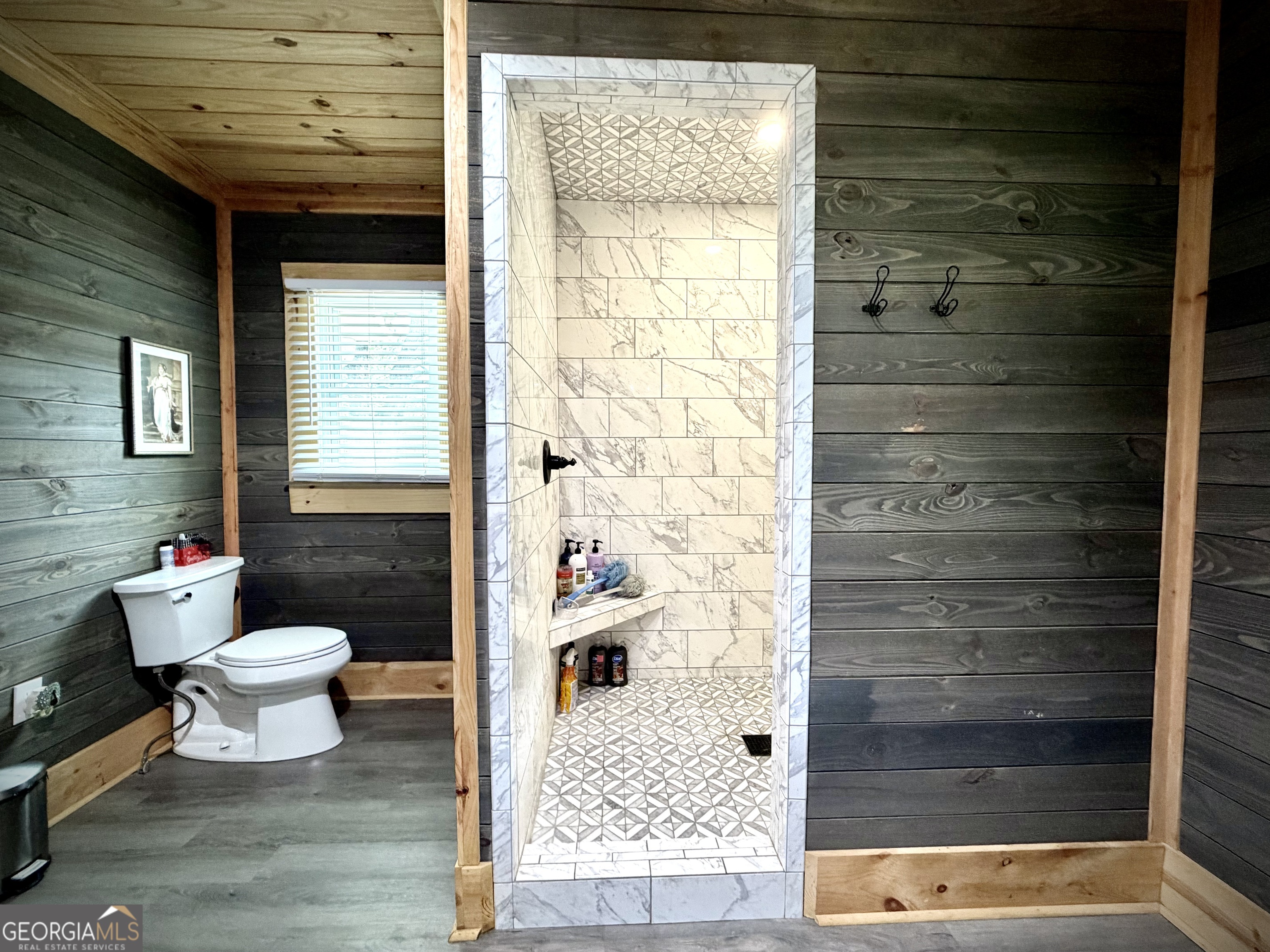 Bathroom with a marble-look walk-in shower, geometric tile floor, and dark wood-plank walls.