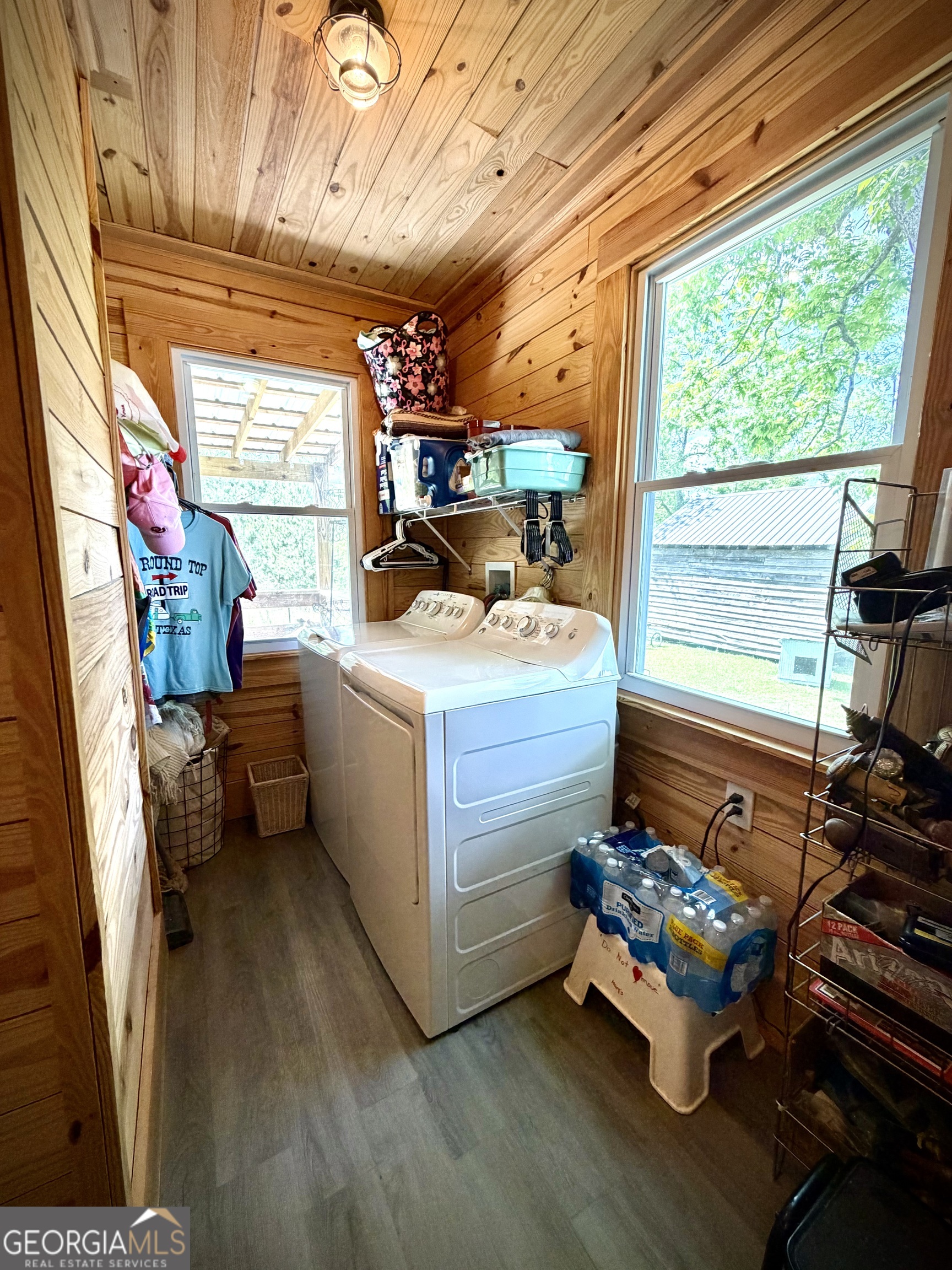 Laundry room with white washer and dryer, wood-paneled walls, and large windows.