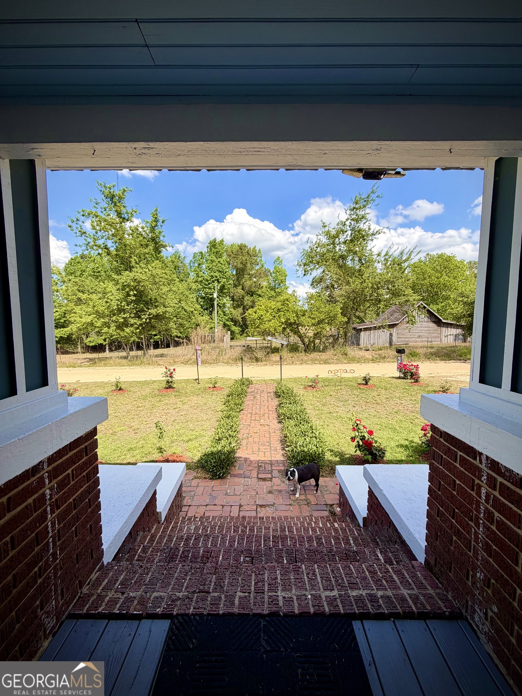 Covered brick porch overlooks a landscaped yard and brick walkway, with a small dog near the steps.