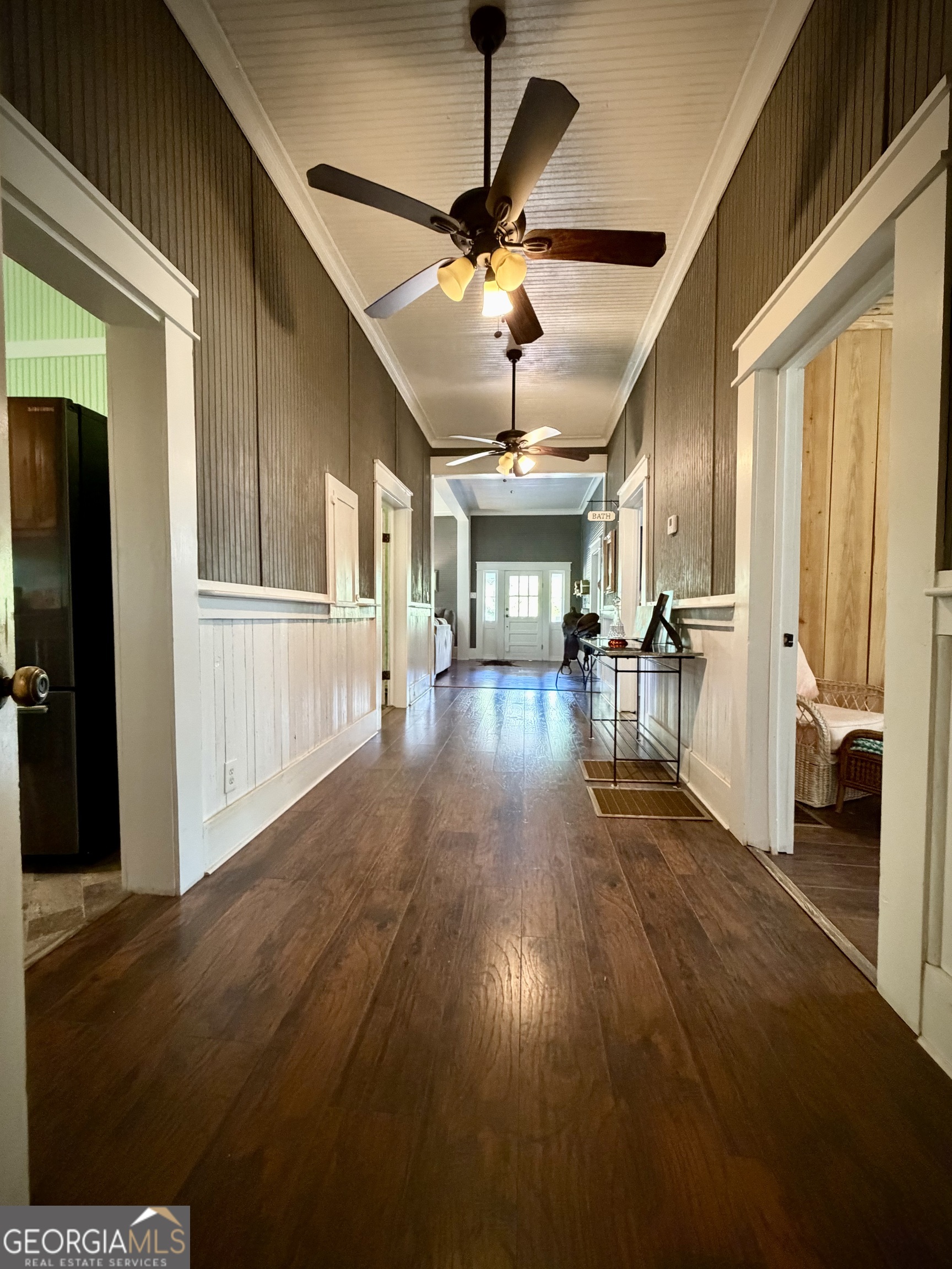 Long hallway with dark wood floors, beadboard walls, two ceiling fans, and a glass-paneled door at the far end.