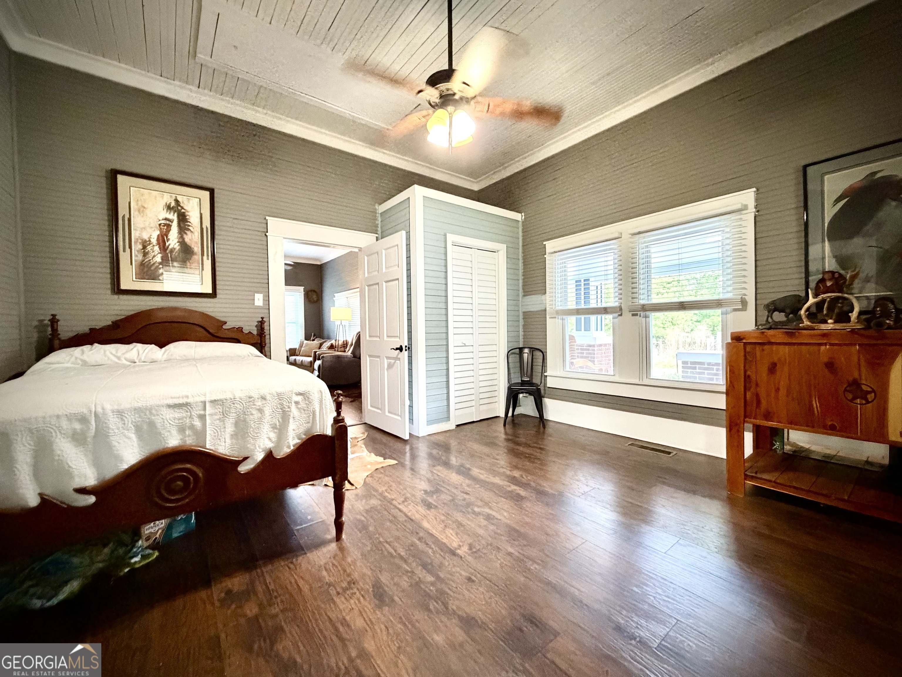 Bedroom with a dark wood bed, louvered closet, and two bright windows.