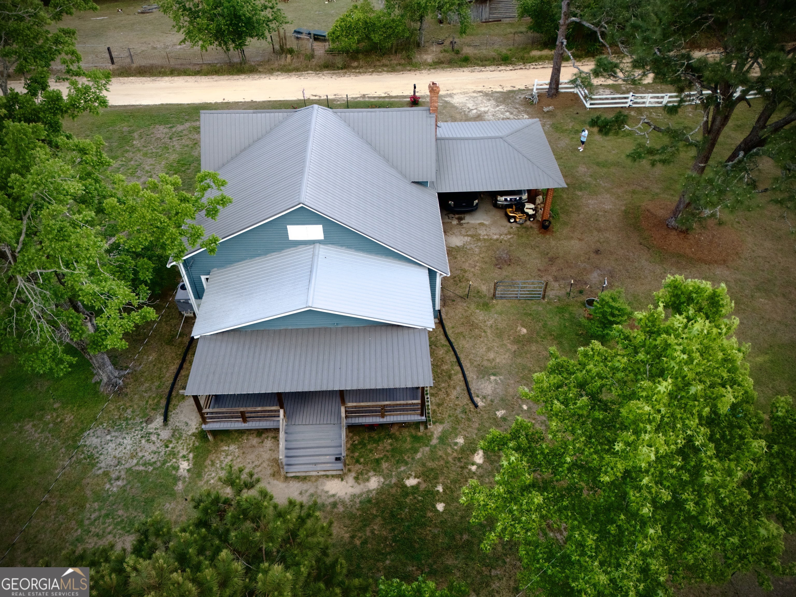 Aerial view of a teal house with gray metal roofs, a covered porch, and an attached carport.