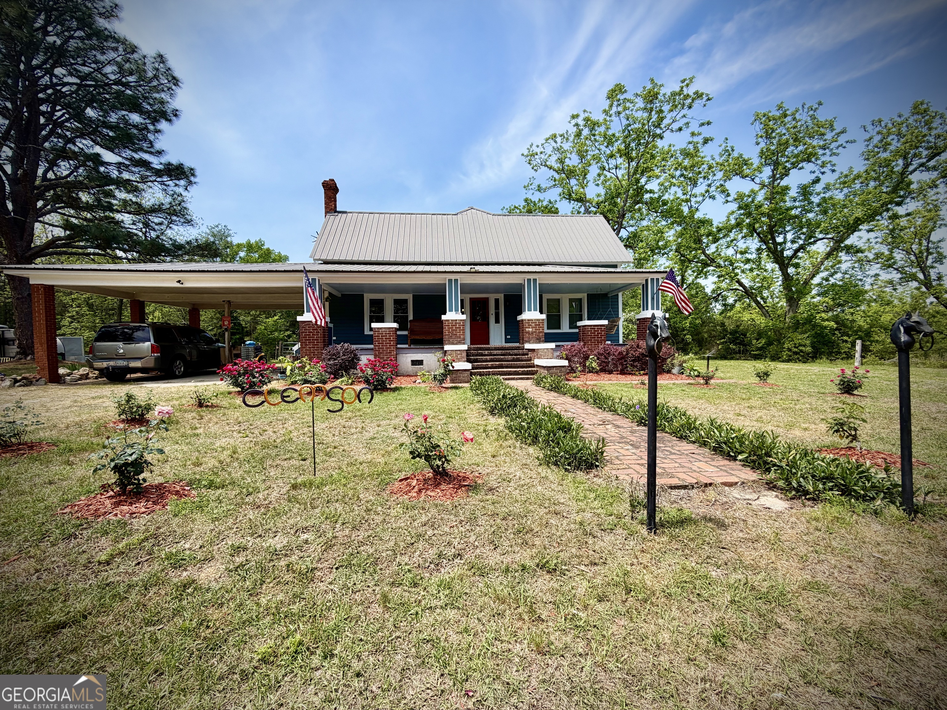 Blue house with a metal roof, brick front steps, carport, and landscaped yard.