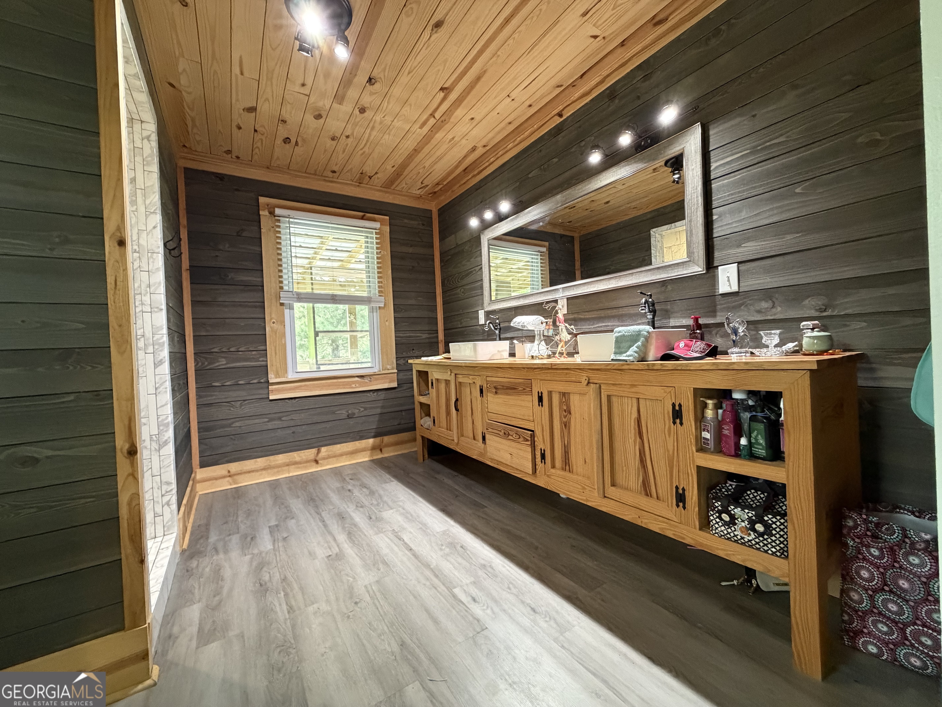 Bathroom with a long wooden vanity, large mirror, and dark plank walls beneath a wood-paneled ceiling.