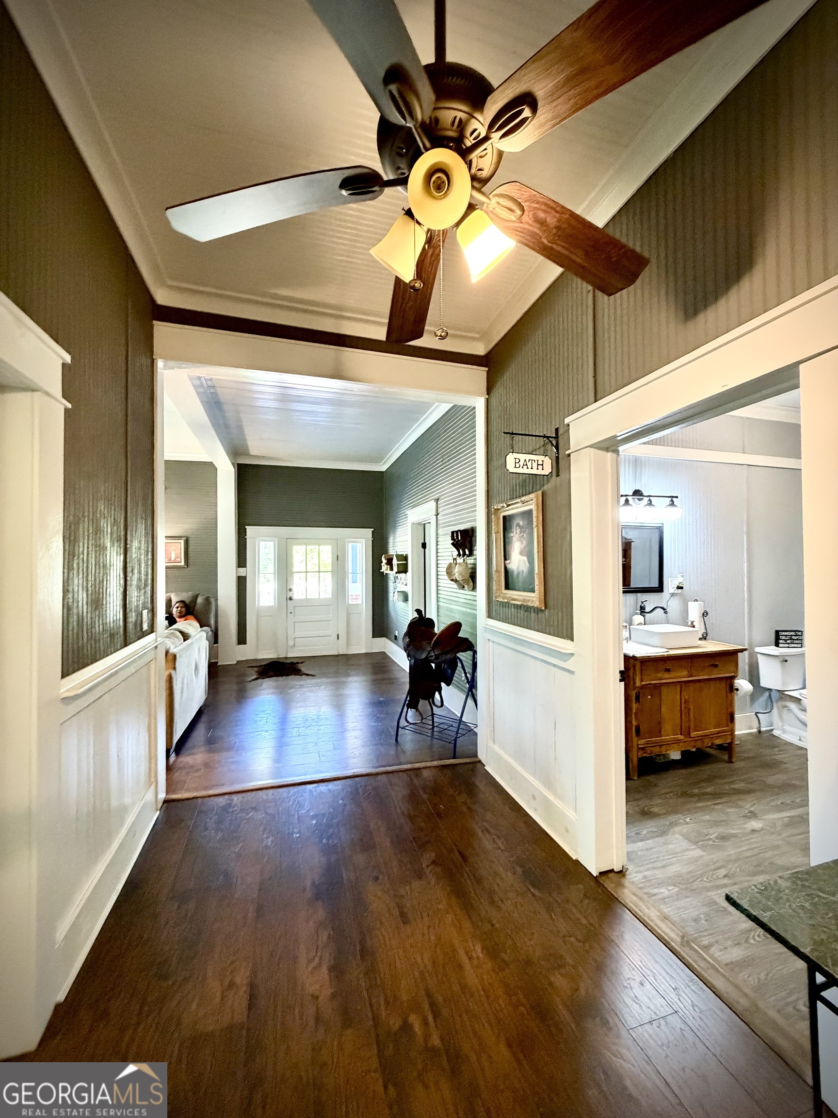 Hallway with dark wood floors, a ceiling fan, and an open doorway to a bathroom with a wooden vanity.