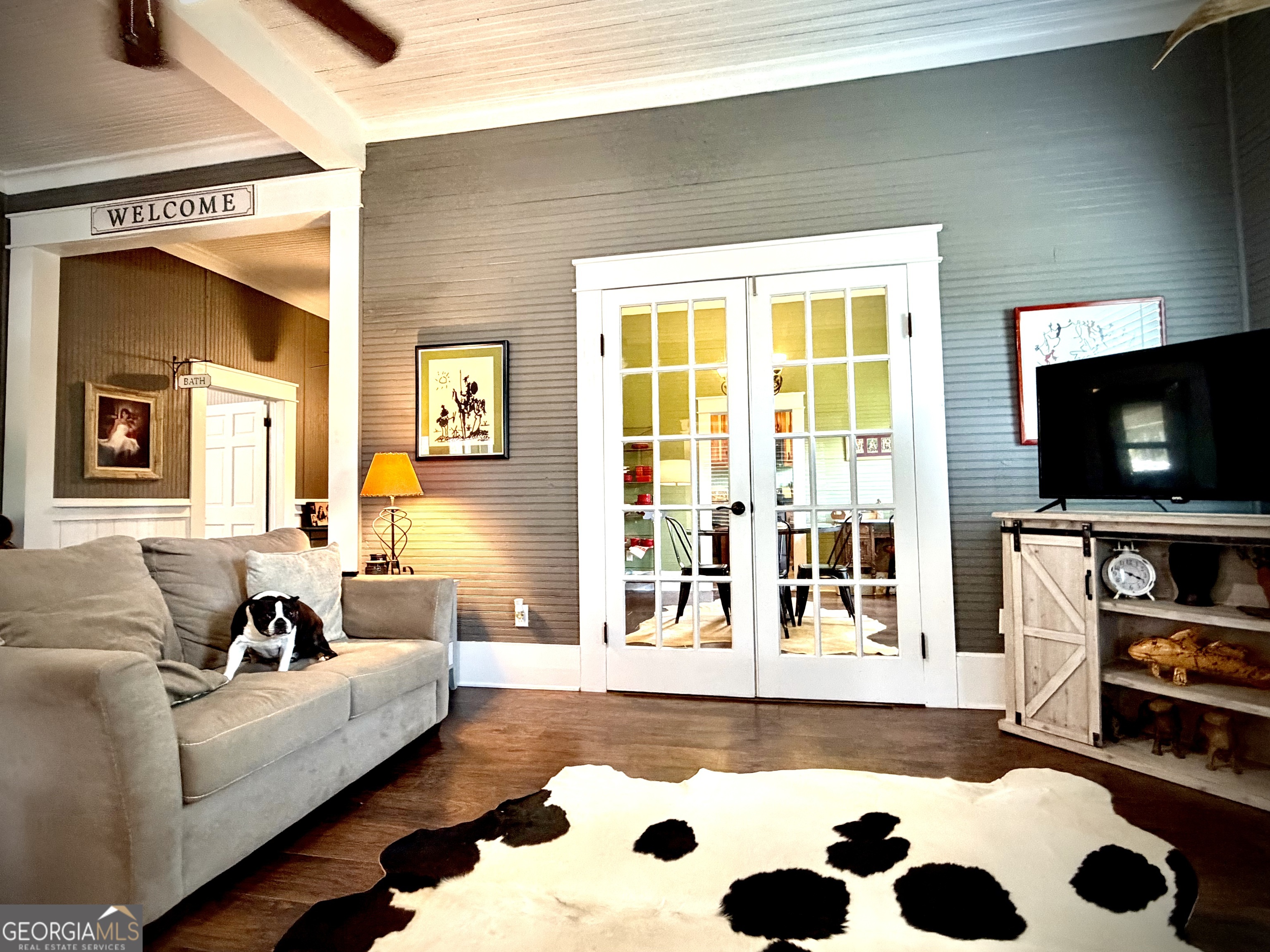 Living room with a gray sectional, a dog, white French doors, and a black-and-white cowhide rug.