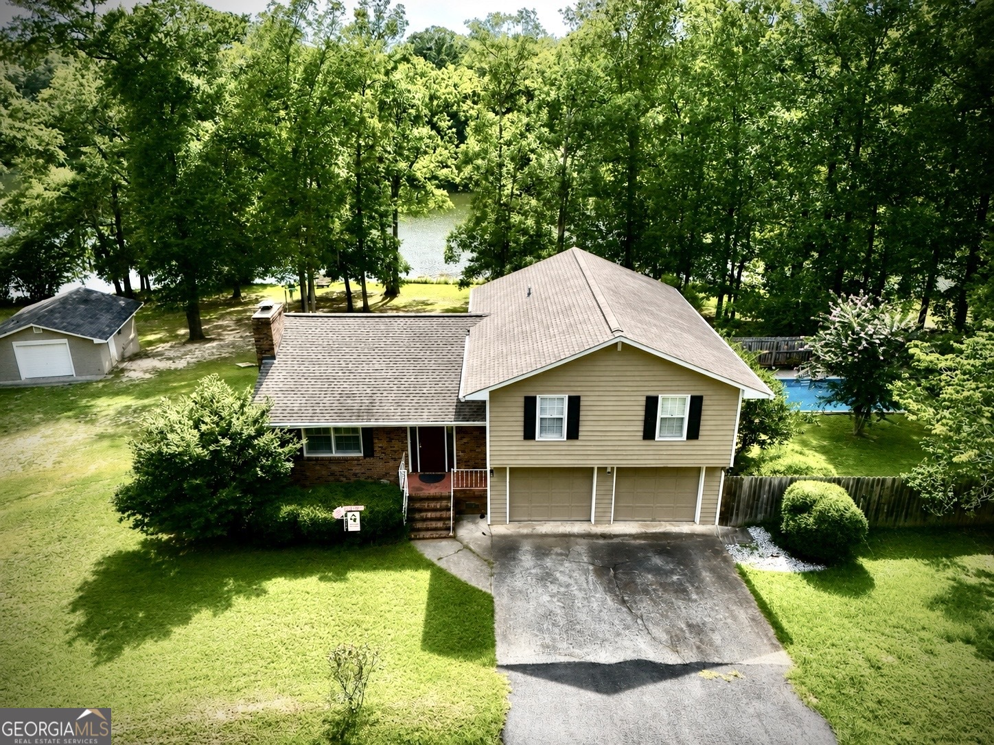 Aerial view of a two-story home with a pool beside a wooded lake.