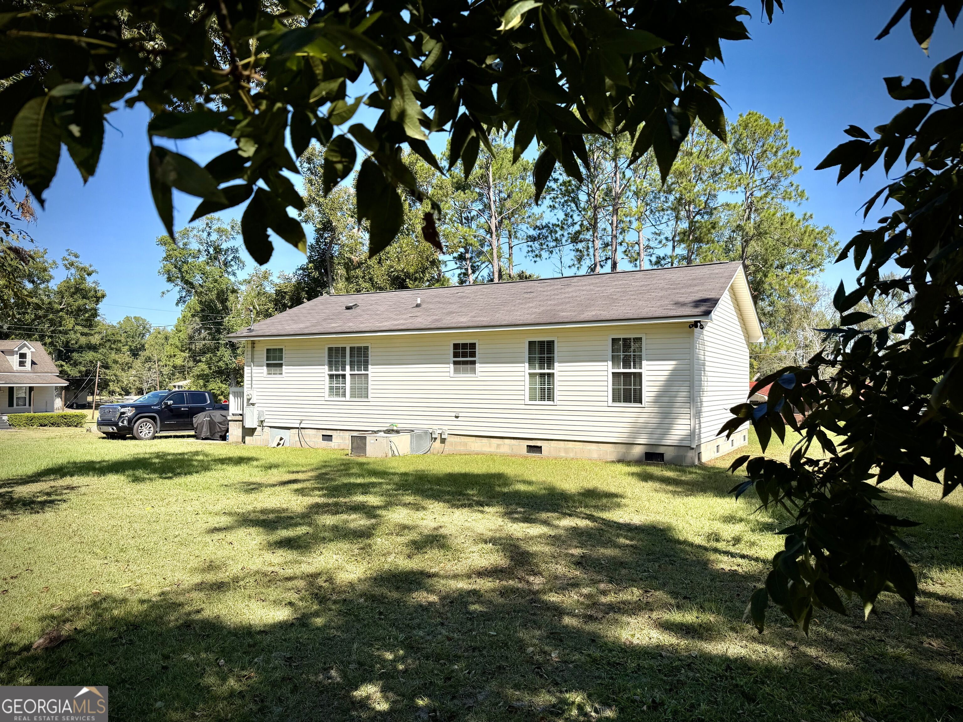 Single-story white house with multiple windows and a broad grassy yard, framed by leafy trees.