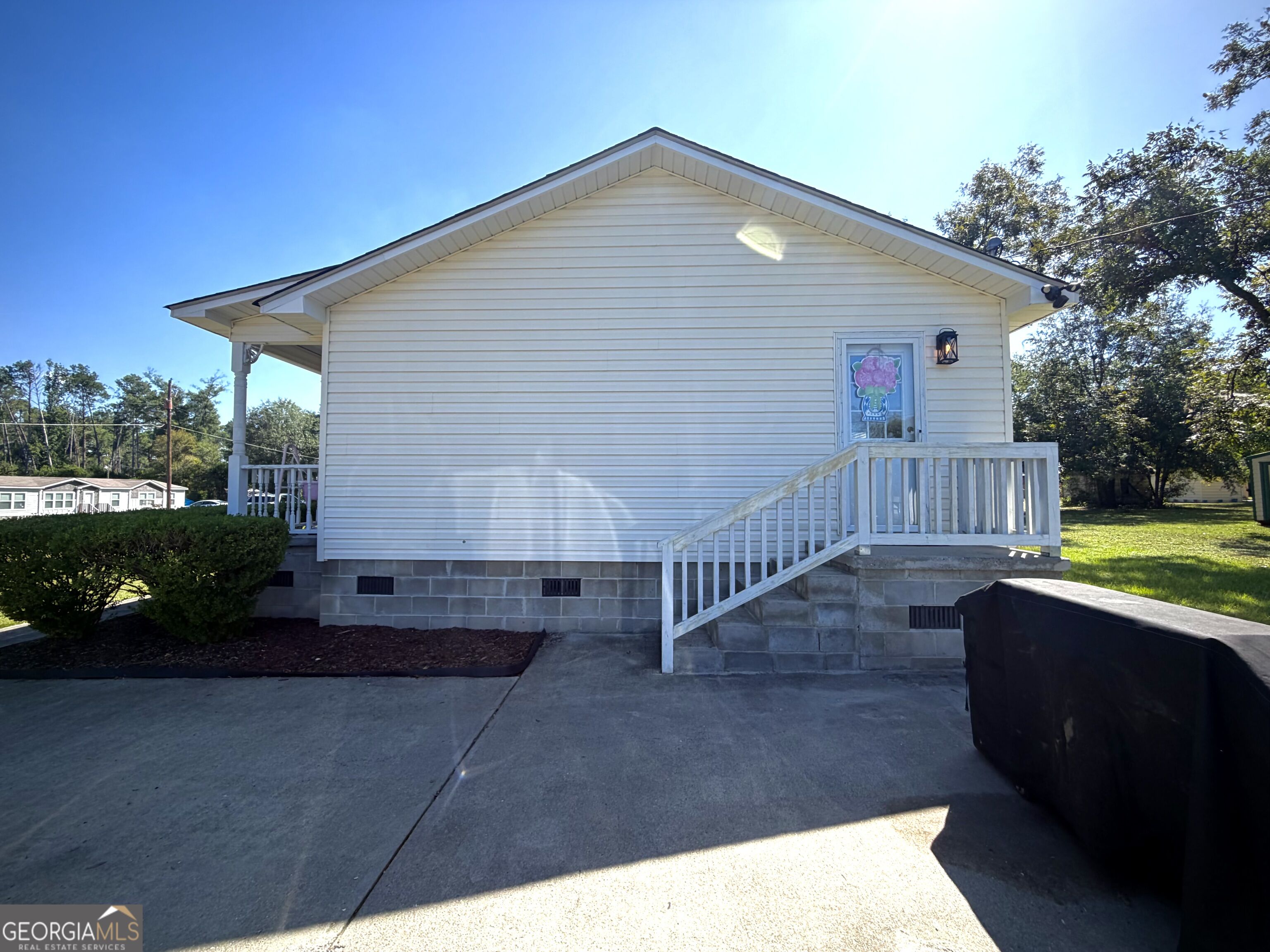 White-sided home with a raised side entry porch, white railings, and concrete driveway.