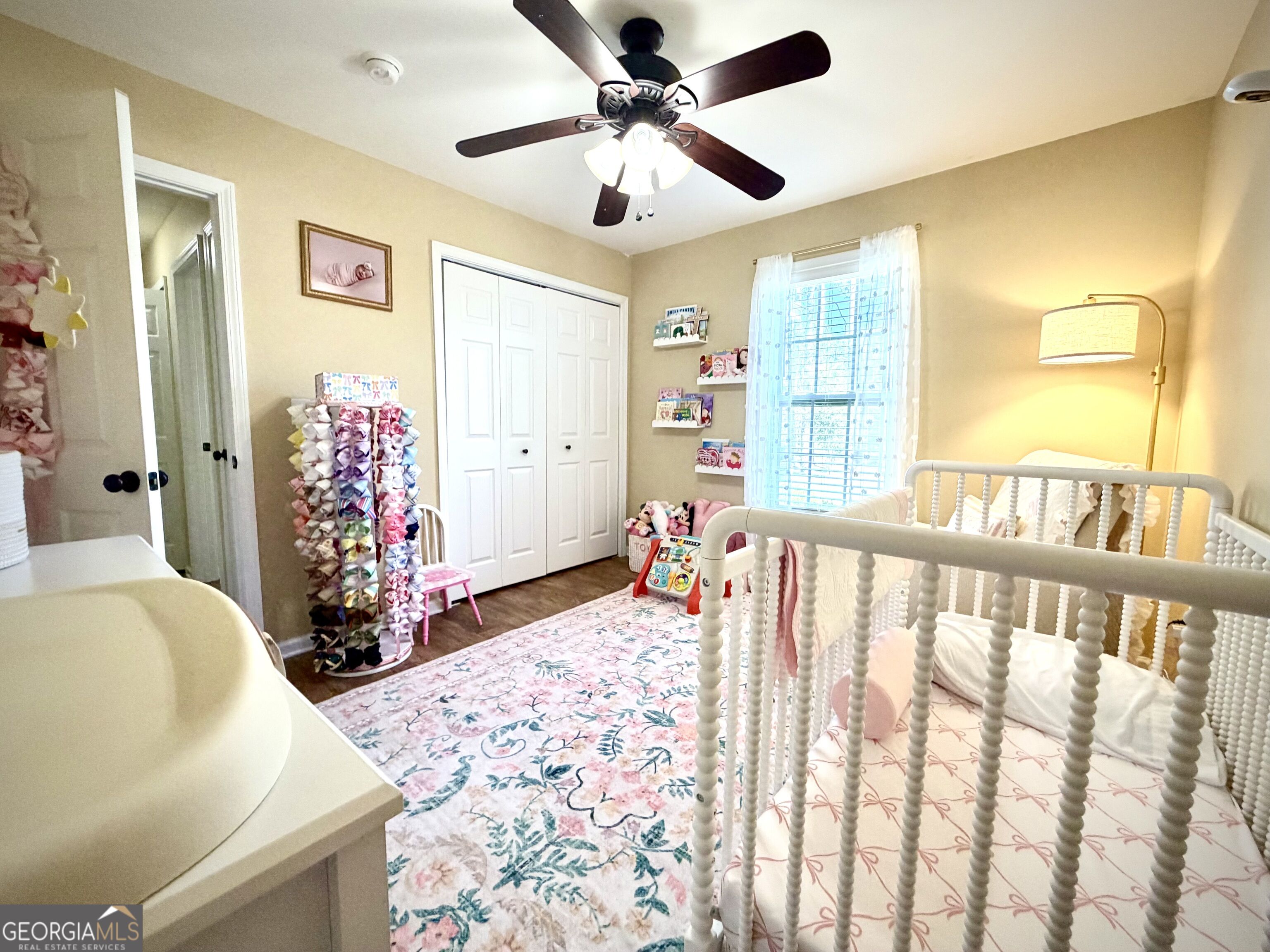 Nursery with a white spindle crib, floral rug, bow rack, and changing table.