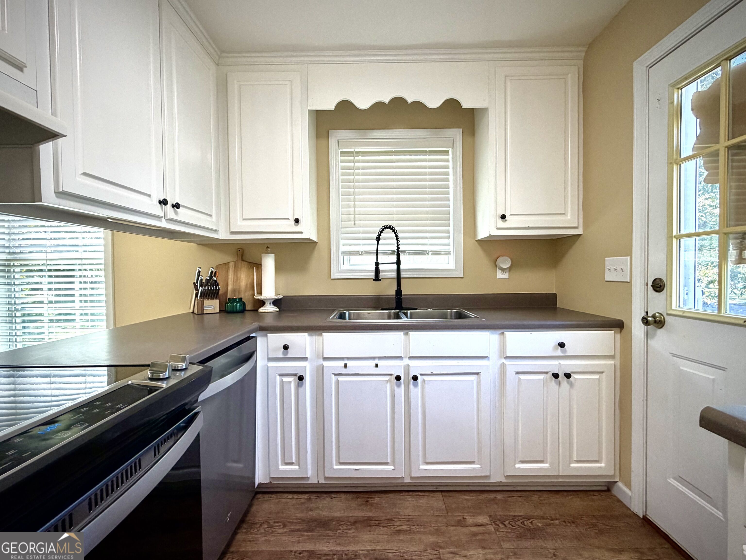 Kitchen with white cabinets, dark countertops, a double sink, and a window above it.