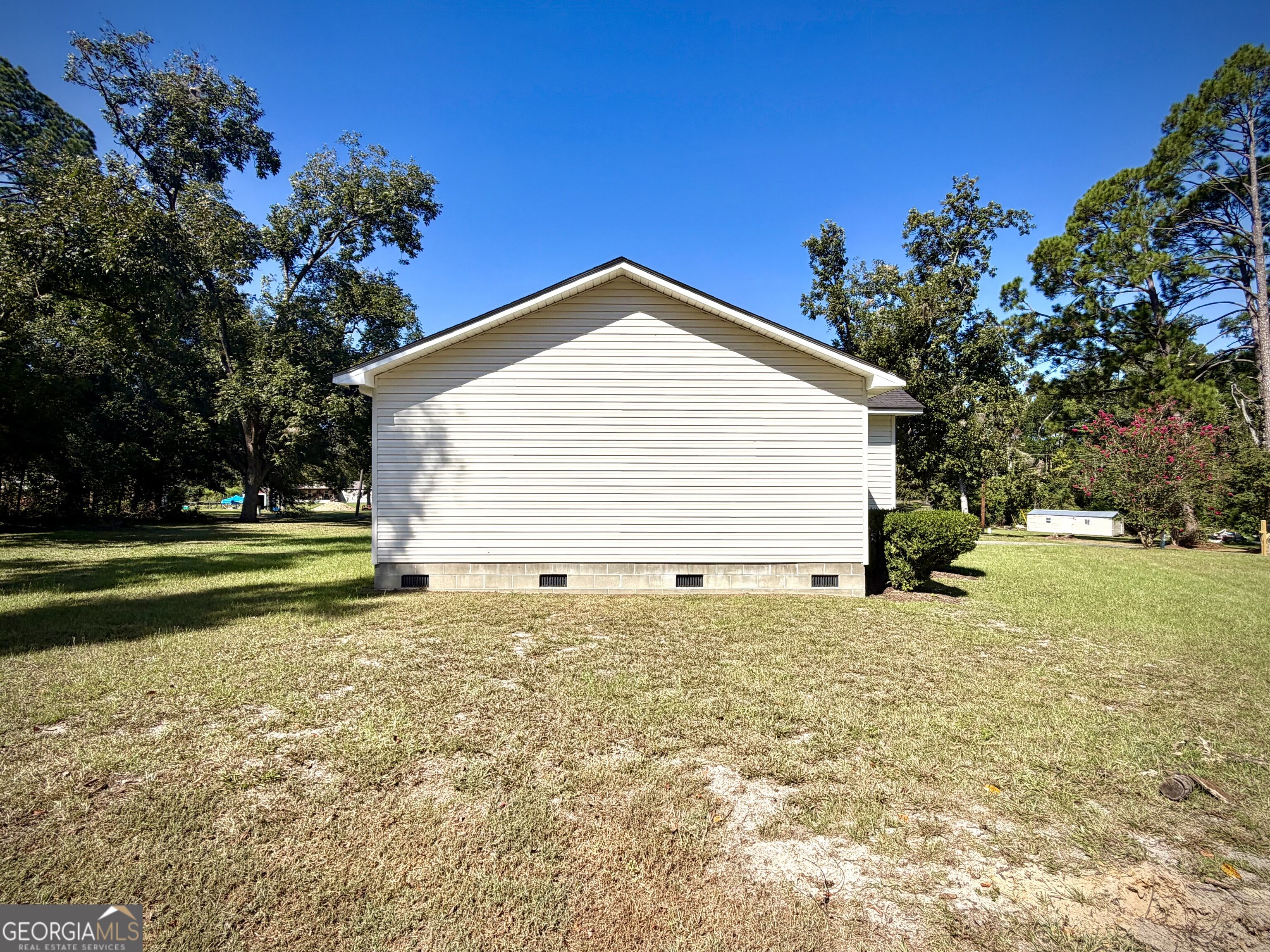 White-sided house’s gable end and grassy yard shaded by mature trees.