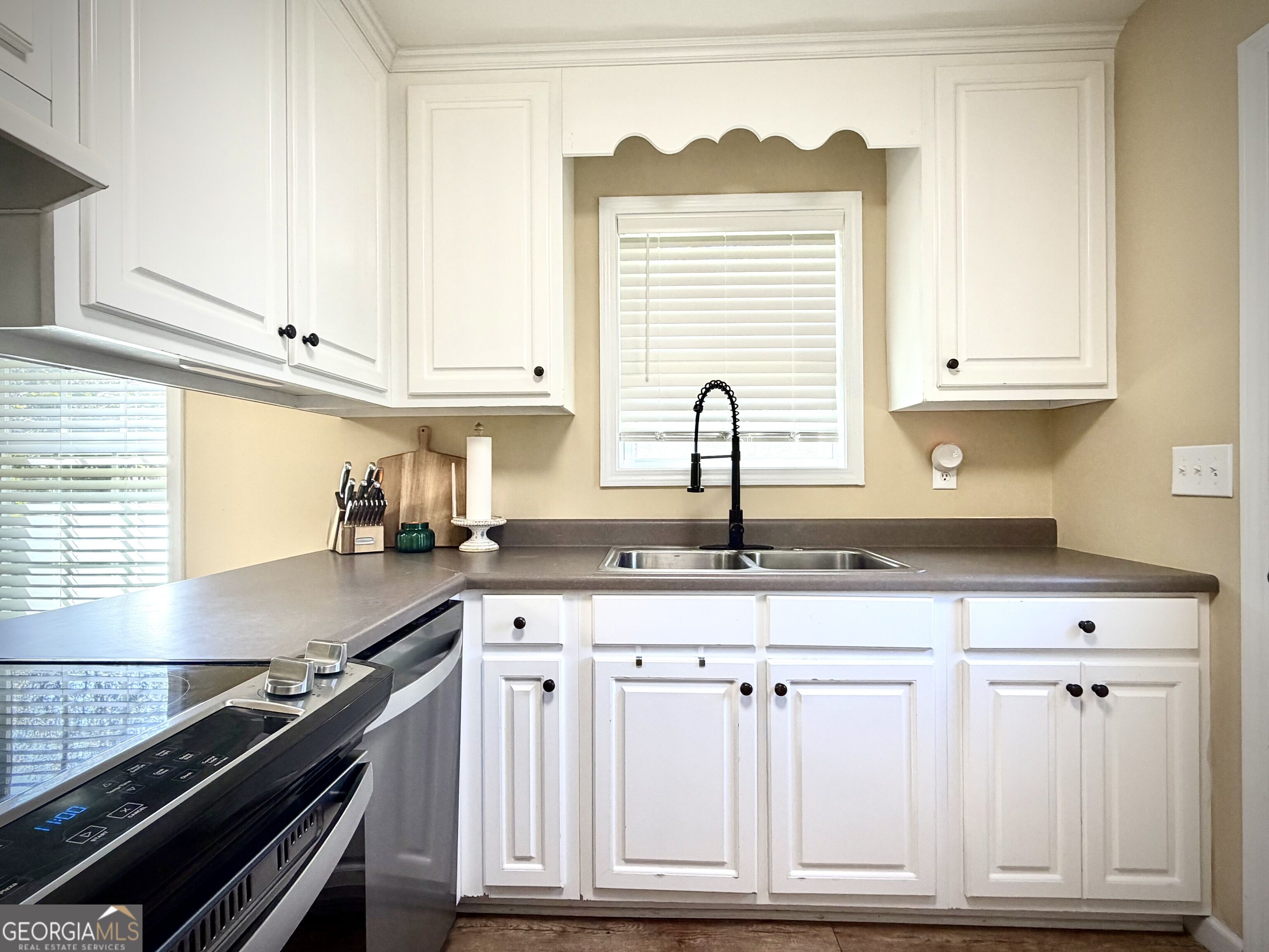 Kitchen with white cabinets, gray countertops, a double sink, and a black range.