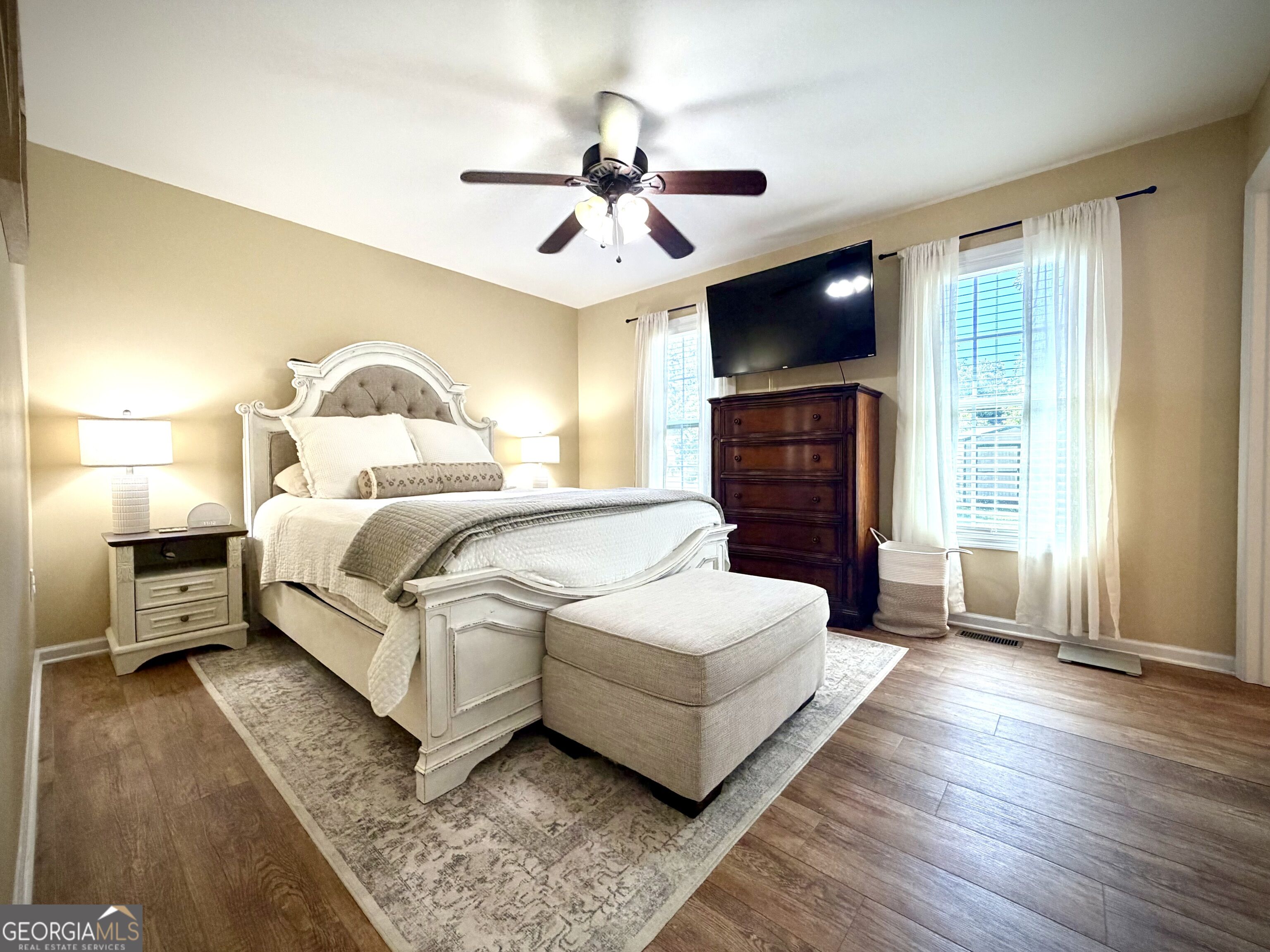 Furnished bedroom with a carved white bed, upholstered bench, and television above a dark dresser.