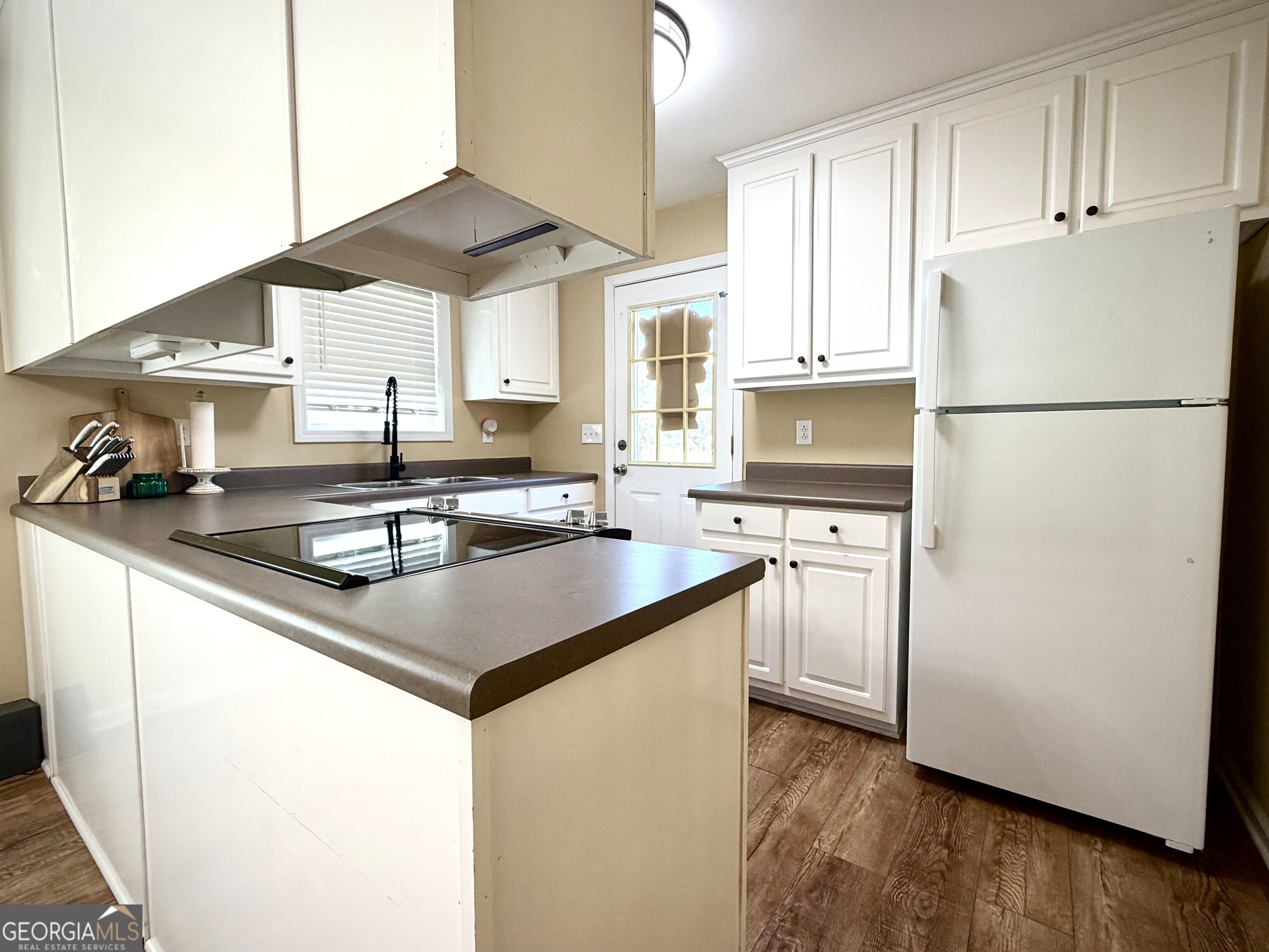 Kitchen with white cabinets, a cooktop peninsula, and wood-look flooring.