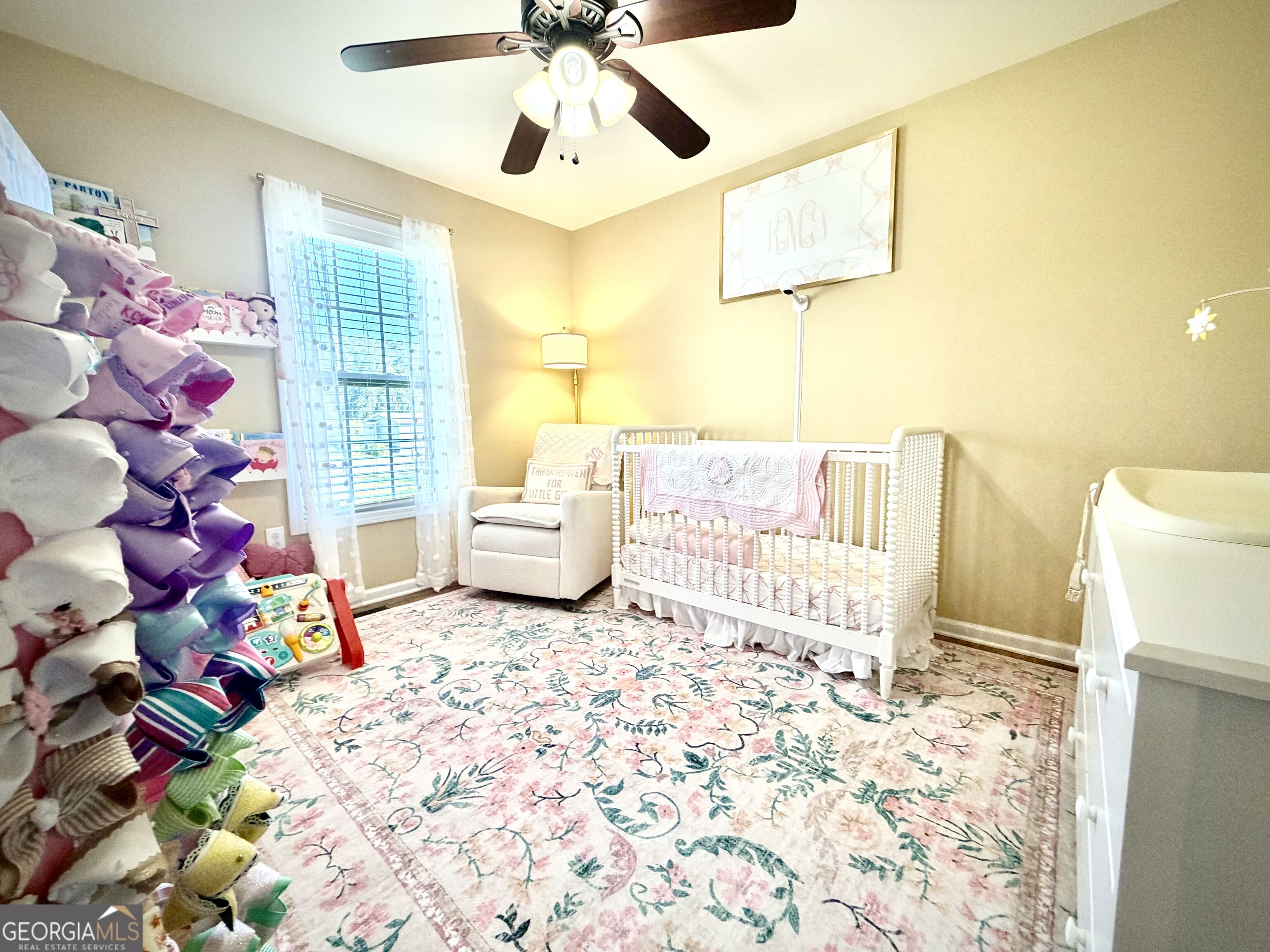 Nursery with a white crib, pink blanket, plush toys, and a large floral rug.