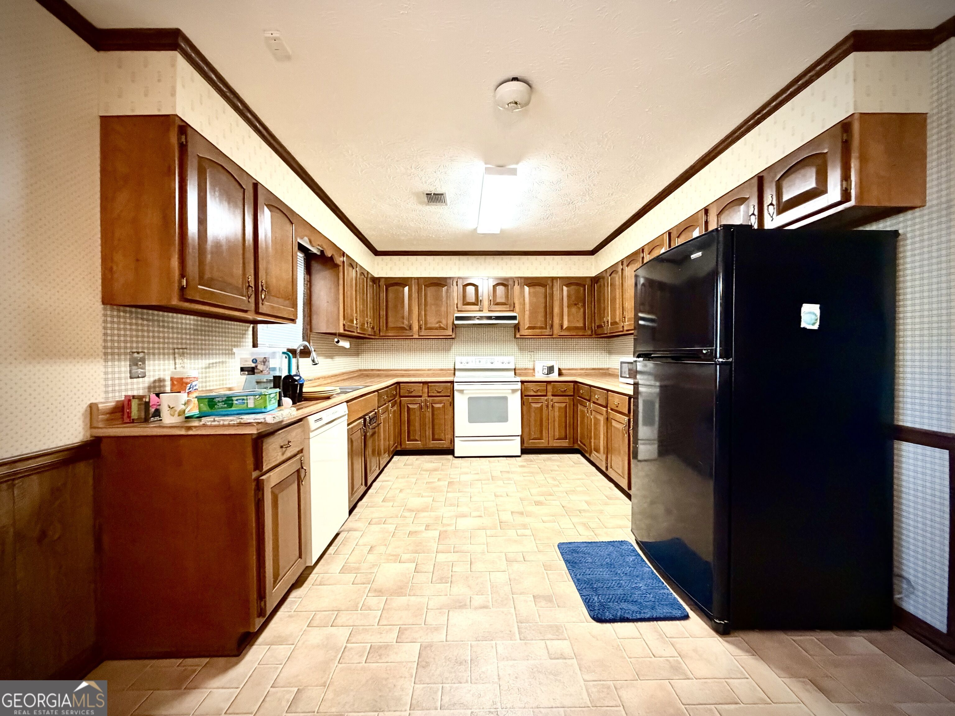 Kitchen with dark wood cabinets, U-shaped counters, tan tile floor, and a large black refrigerator.