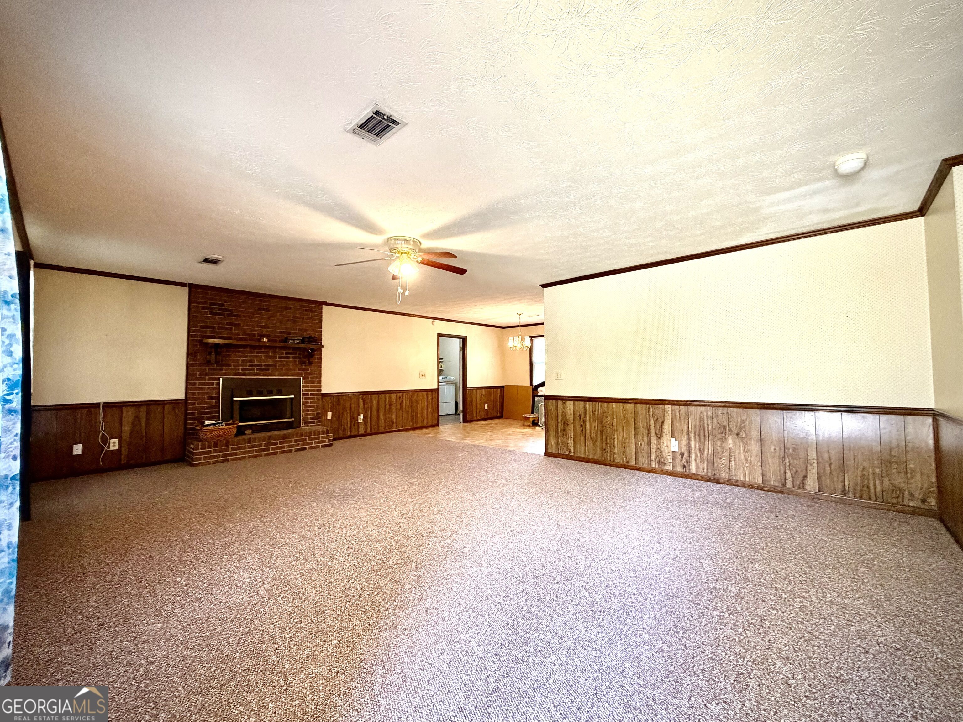 Vacant living room with a brick fireplace, brown carpet, wood-paneled walls, and a ceiling fan.